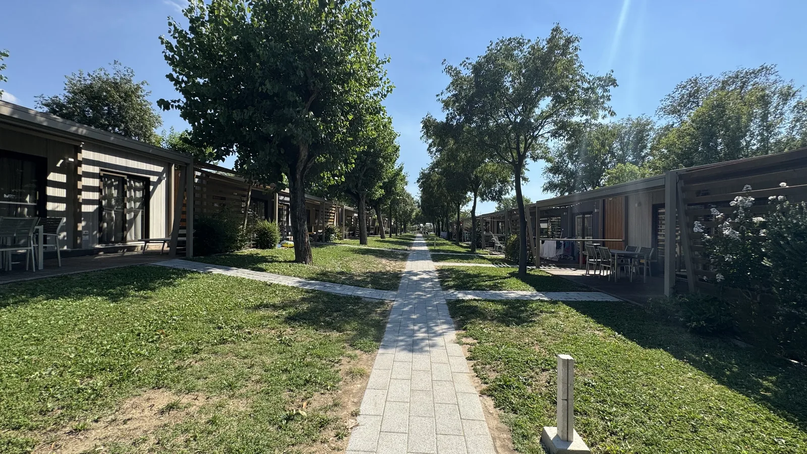 Gepflasterter Weg zwischen Reihen moderner Mobilheime mit Holz-Pergolen am Camping La Quercia