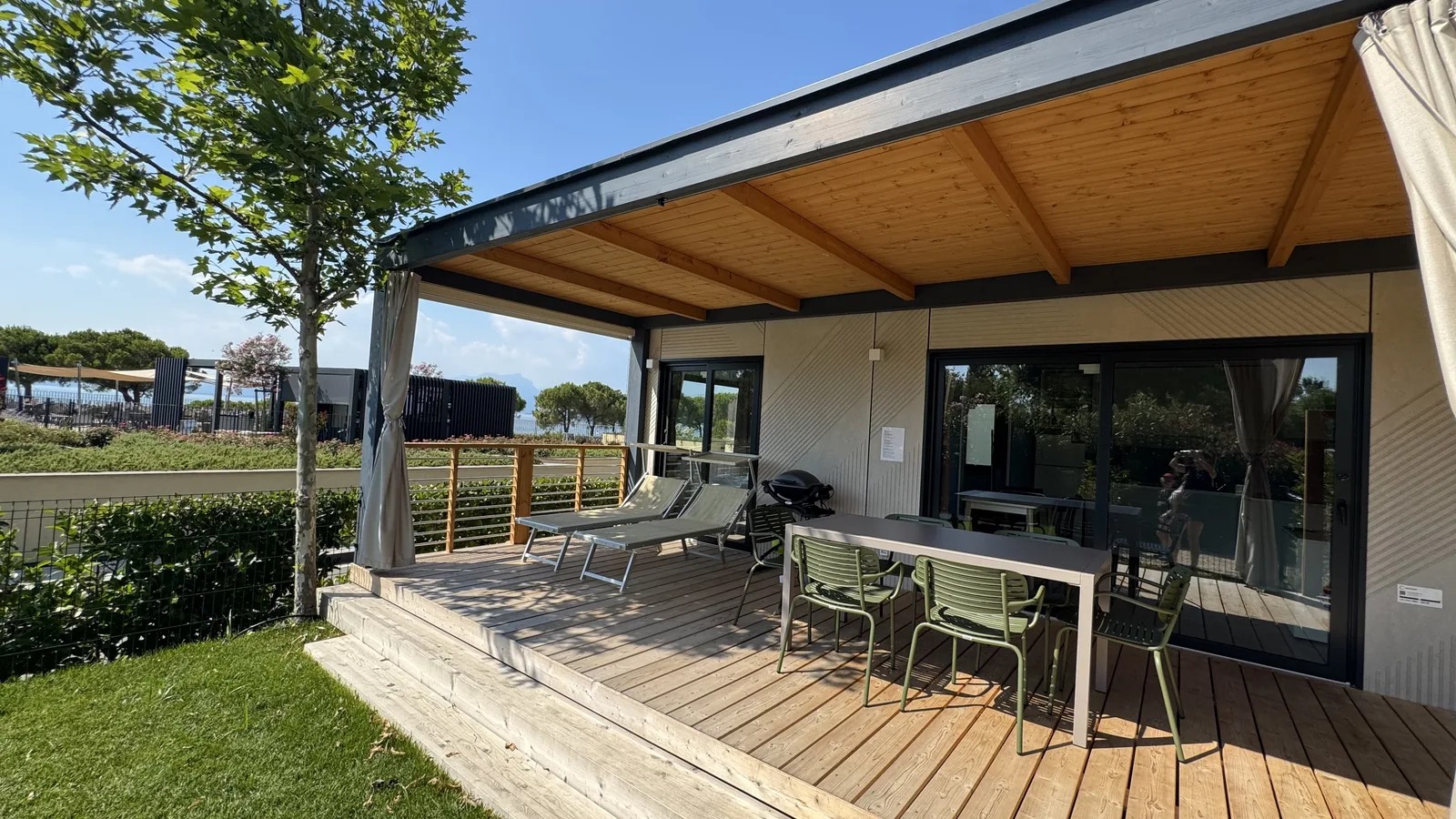 Modernes Mobilheim mit überdachter Holzterrasse, Esstisch, Liegen und Gasgrill am Camping La Quercia