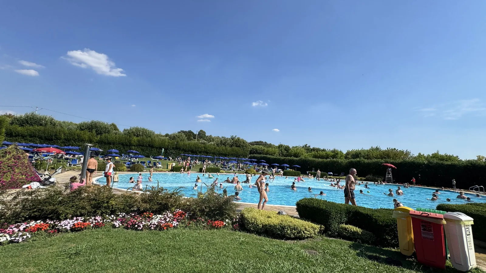 Große geschwungene Poollandschaft mit blauen Sonnenschirmen und Liegewiese am Camping La Quercia