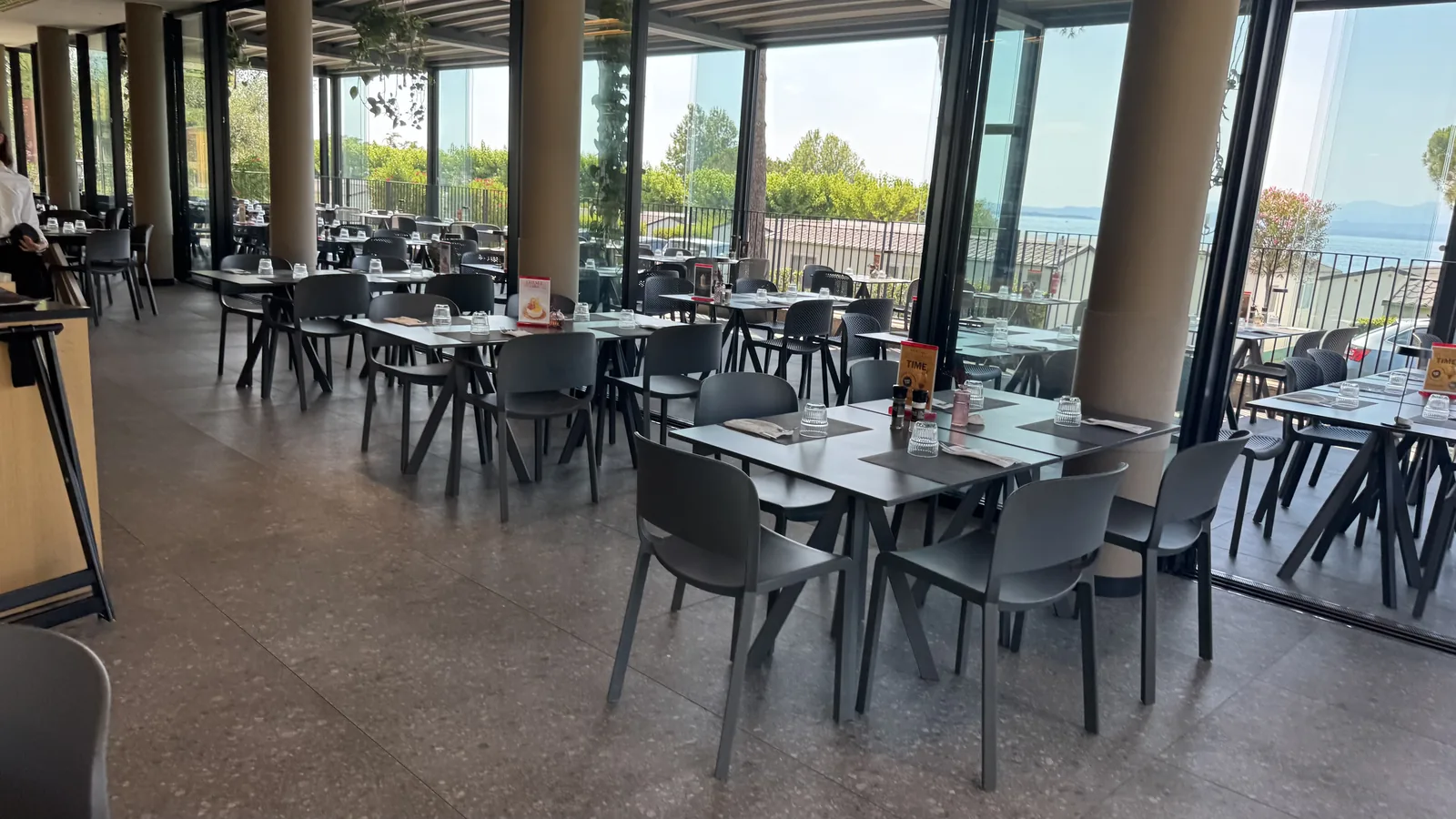 Restaurant mit komplett geöffneter Glasfront und gedeckten Tischen mit Blick auf den Gardasee