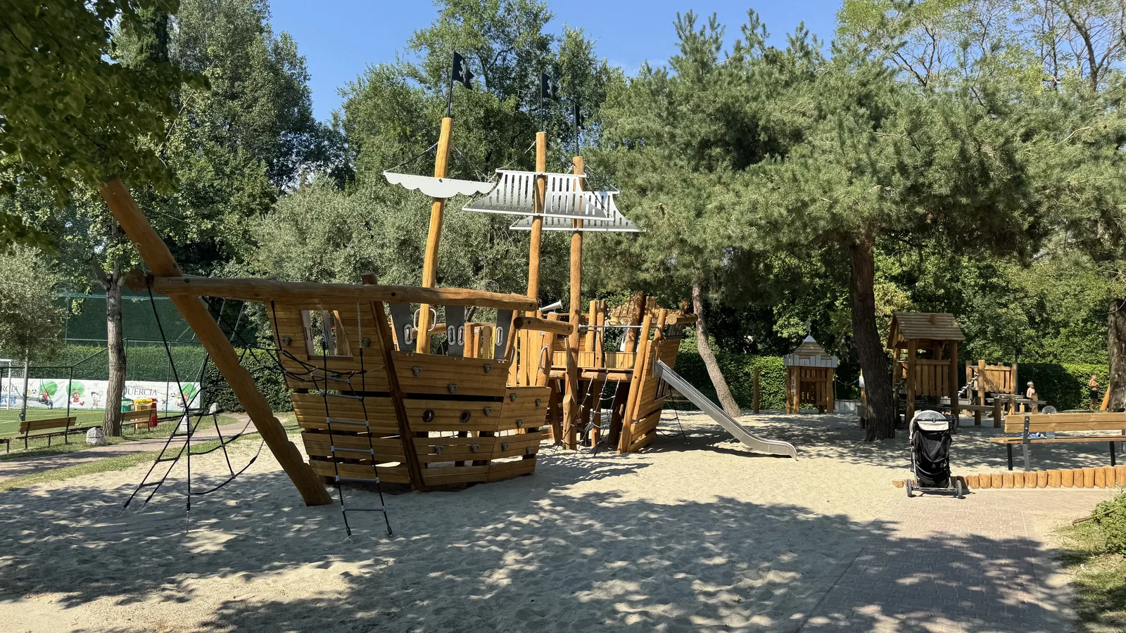 Großes Holz-Piratenschiff mit Kletternetz und Rutsche auf Sand unter Pinien am Camping La Quercia