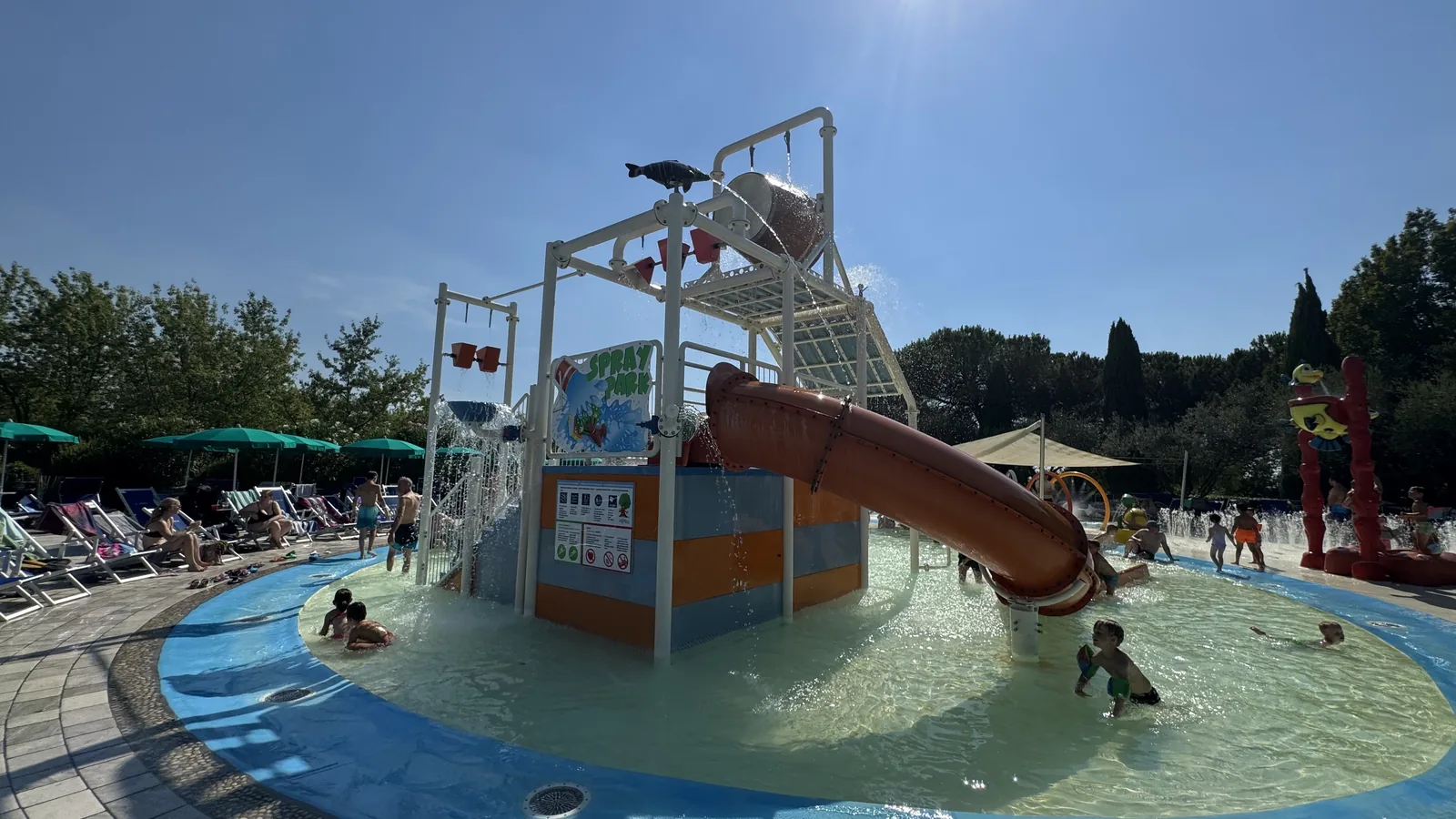 Spray Park mit Kippeimer, Spritzdüsen und kleiner Röhrenrutsche in einem knietiefen Rundbecken