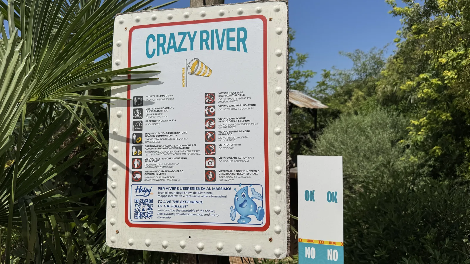 Regeltafel der Attraktion Crazy River mit Piktogrammen und der Angabe Mindestgröße 130 cm, rechts daneben eine Messlatte mit OK- und NO-Markierung