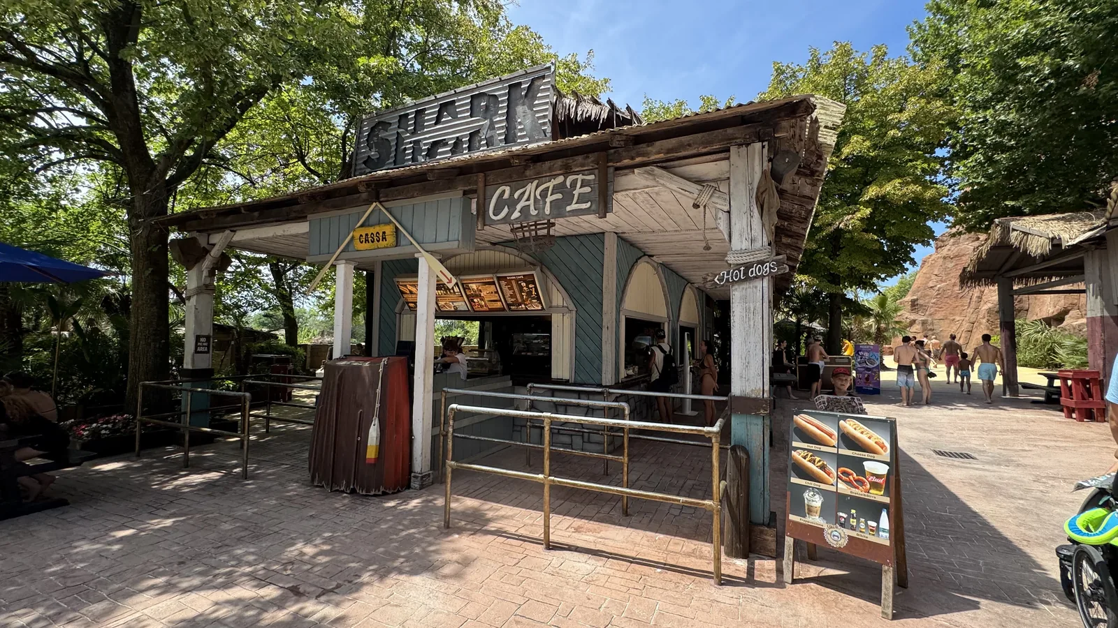 Imbissbude aus verwittertem Holz mit dem Schriftzug Shark Cafe, davor Absperrgitter und eine Aufsteller-Tafel mit Hot Dogs