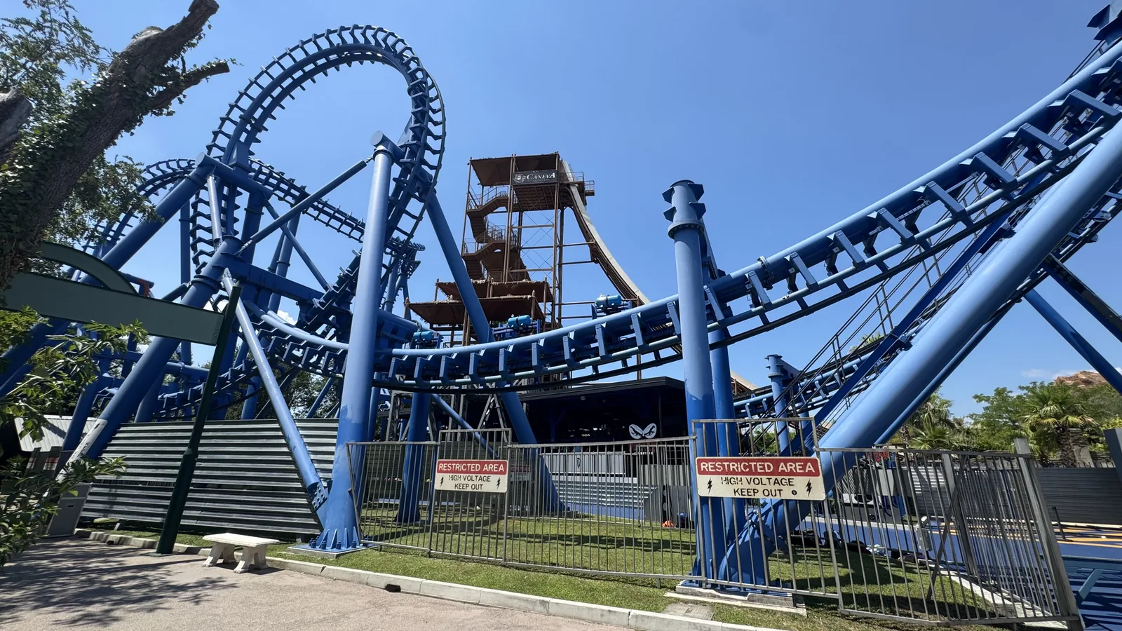 Blaue Stahlachterbahn mit Looping und Schraube vor wolkenlosem Himmel im Movieland Park