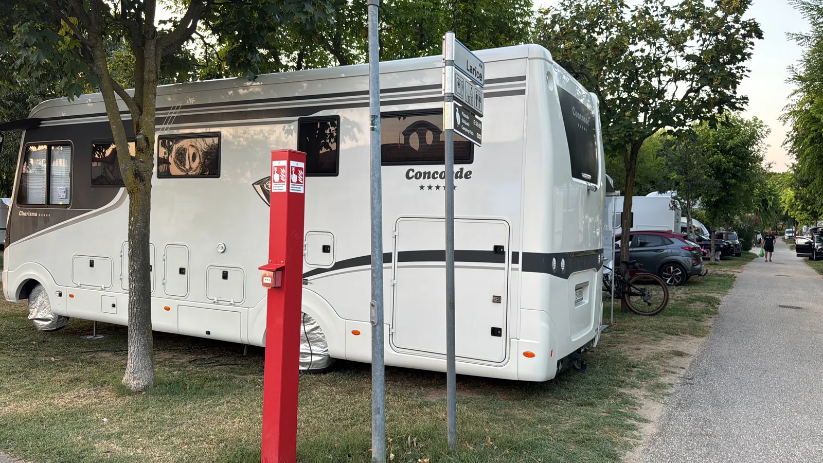 Reisemobil auf einem Rasenstellplatz mit roter Versorgungssäule und Wegweiser mit der Aufschrift Larice