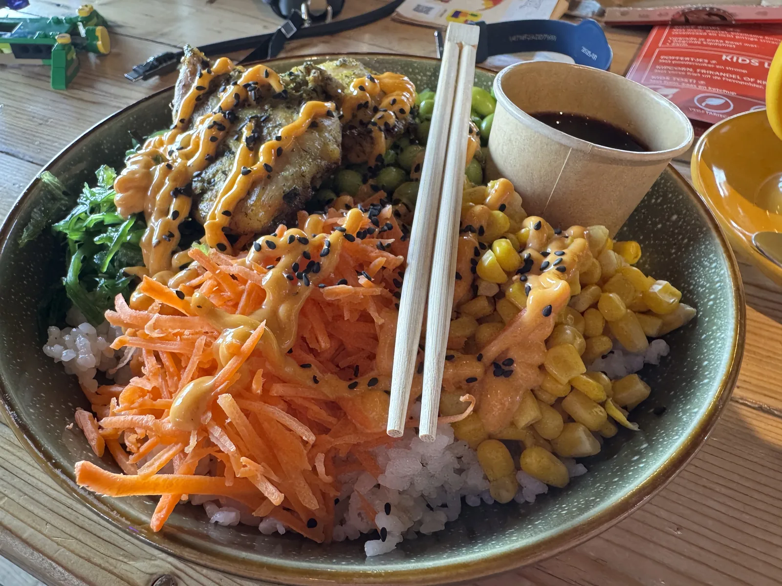 Große Bowl mit Reis, Karottenstreifen, Pommes und Sauce, daneben Stäbchen und eine Speisekarte