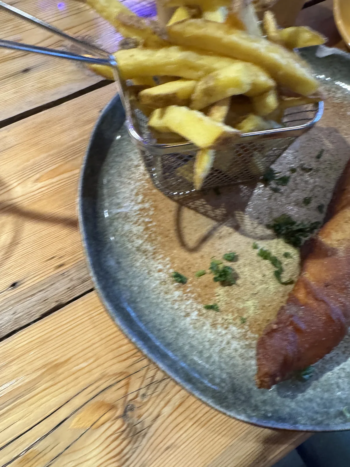 Teller mit frittiertem Fisch und einem Pommes-Körbchen auf einem Holztisch im Beachclub