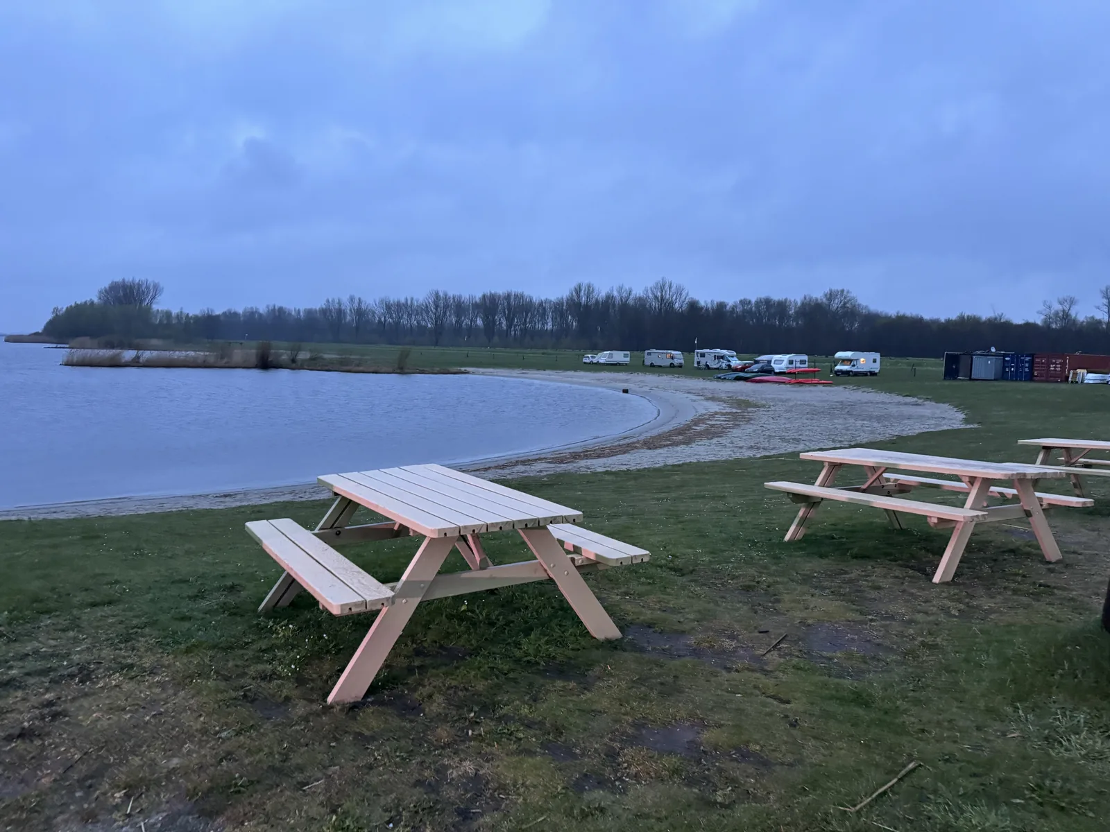 Wiese mit hellen Picknicktischen direkt am Ufer in der Dämmerung