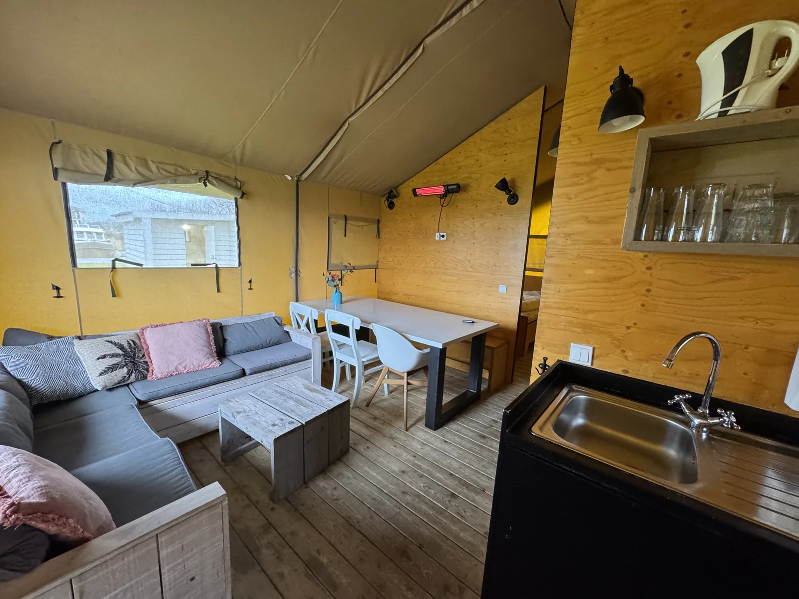 Innenraum eines Safari-Zeltes auf Camping Marina Eemhof mit Sofa, Esstisch und Küchenzeile vor einer gelb gestrichenen Holzwand