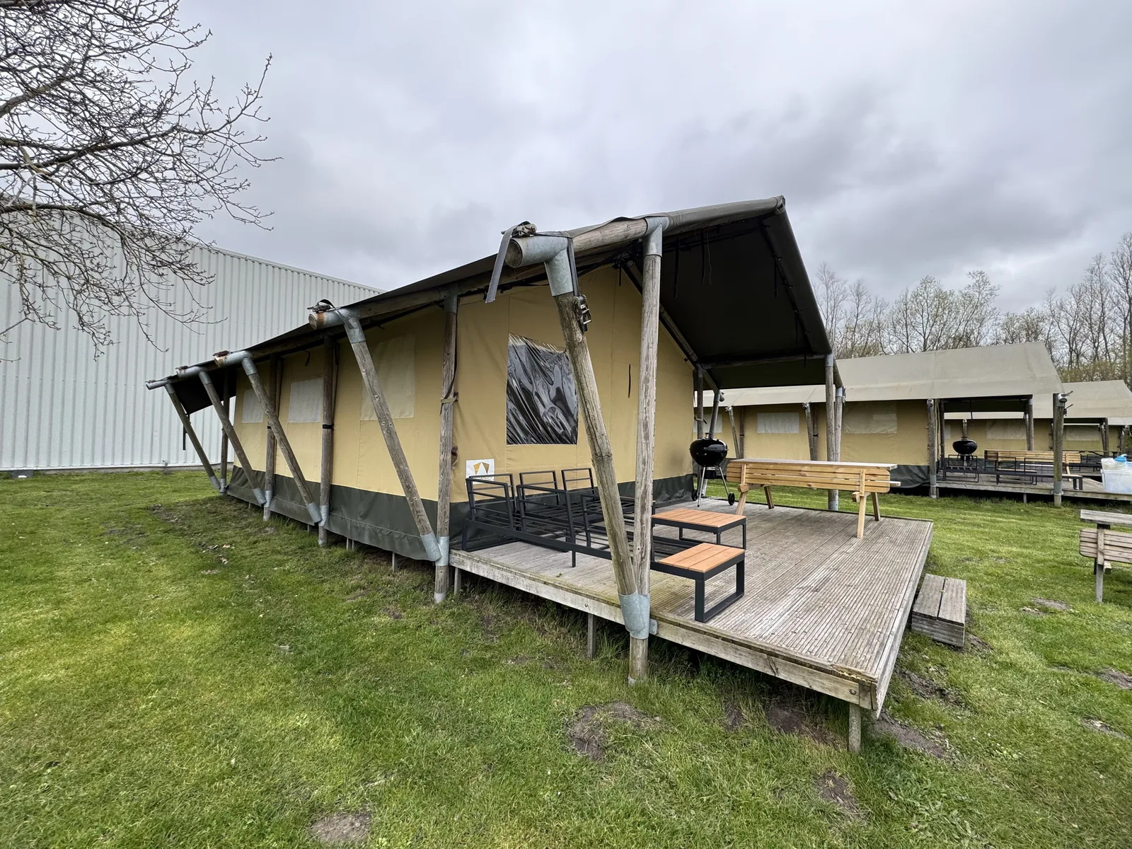 Reihe von Safari-Zelten mit Holzterrassen und Gartenmöbeln auf der Wiese von Camping Marina Eemhof unter grauem Aprilhimmel