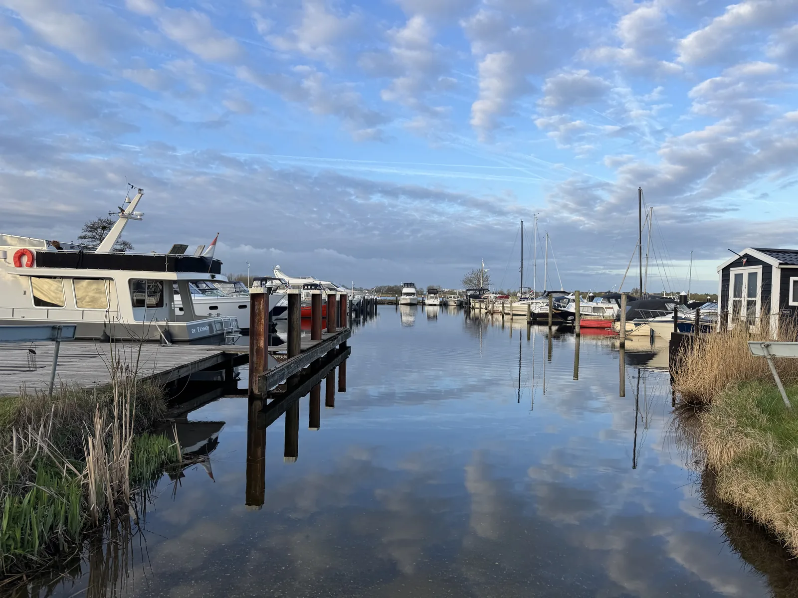 Yachthafenbecken mit Motorbooten am Steg, spiegelglattes Wasser und Federwolken am Himmel