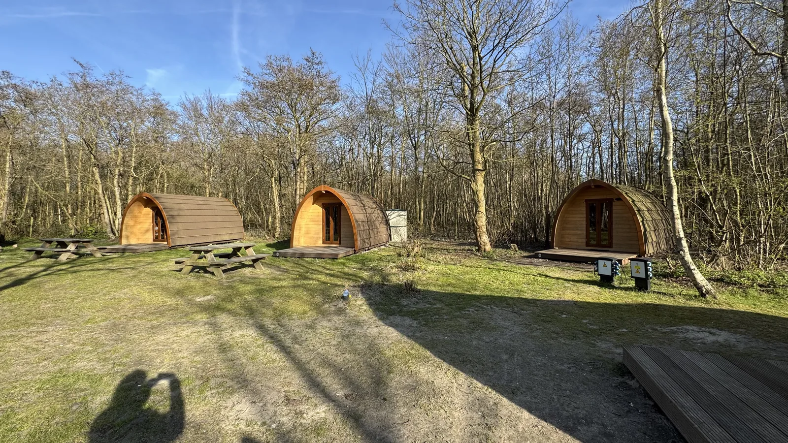 Drei Campingfässer in lockerer Reihe auf der Wiese, jeweils mit eigener Terrasse und Bank