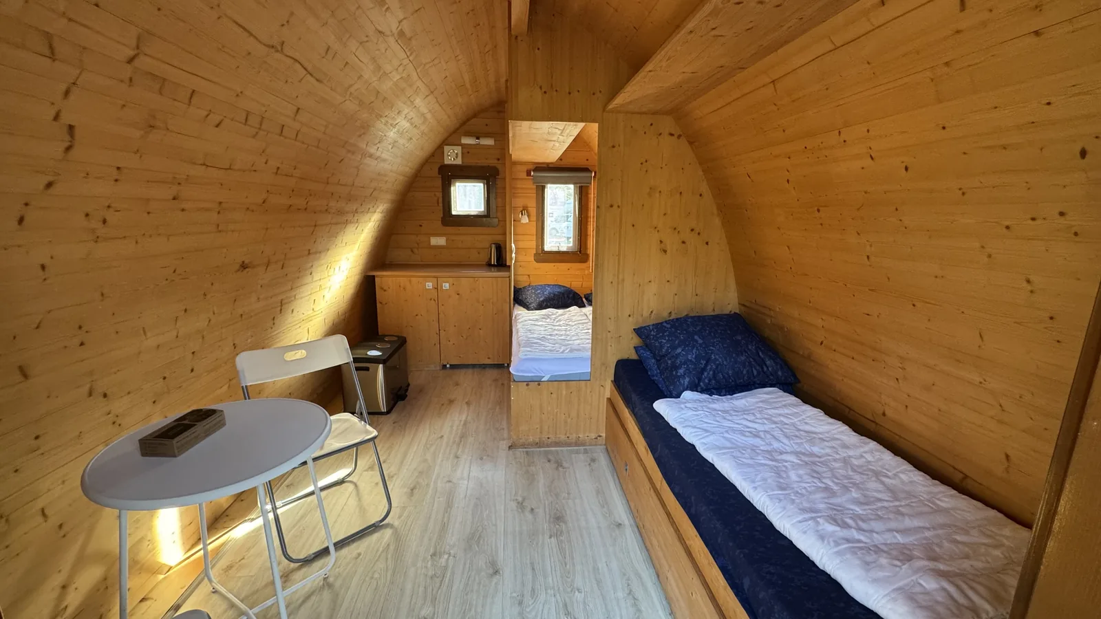Innenraum eines hölzernen Campingfasses mit Bett, kleinem Tisch und Einbauschrank