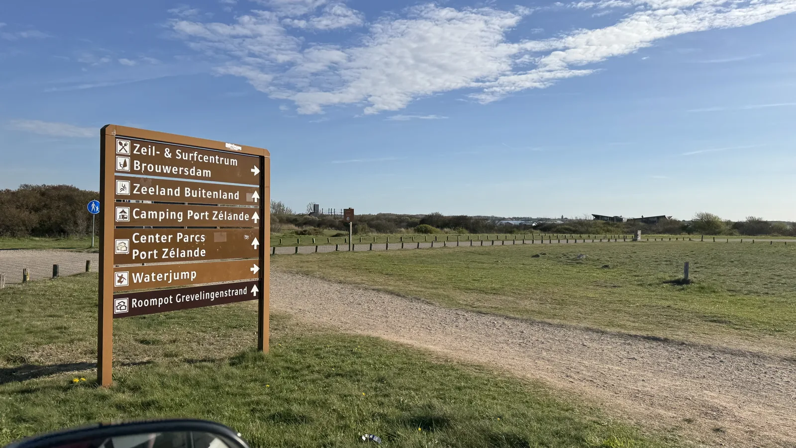 Hölzerner Wegweiser an einer offenen Feldkreuzung mit den Zielen Zeil- und Surfcentrum Brouwersdam, Camping Port Zélande, Center Parcs Port Zélande, Waterjump und Grevelingenstrand