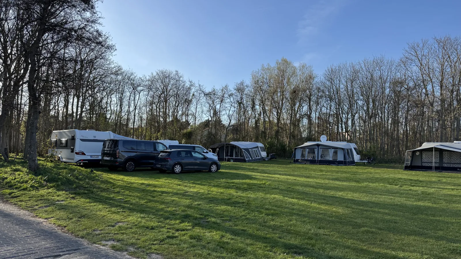 Weite Rasenfläche, am hinteren Rand eine Reihe Wohnwagen mit Vorzelten und Autos