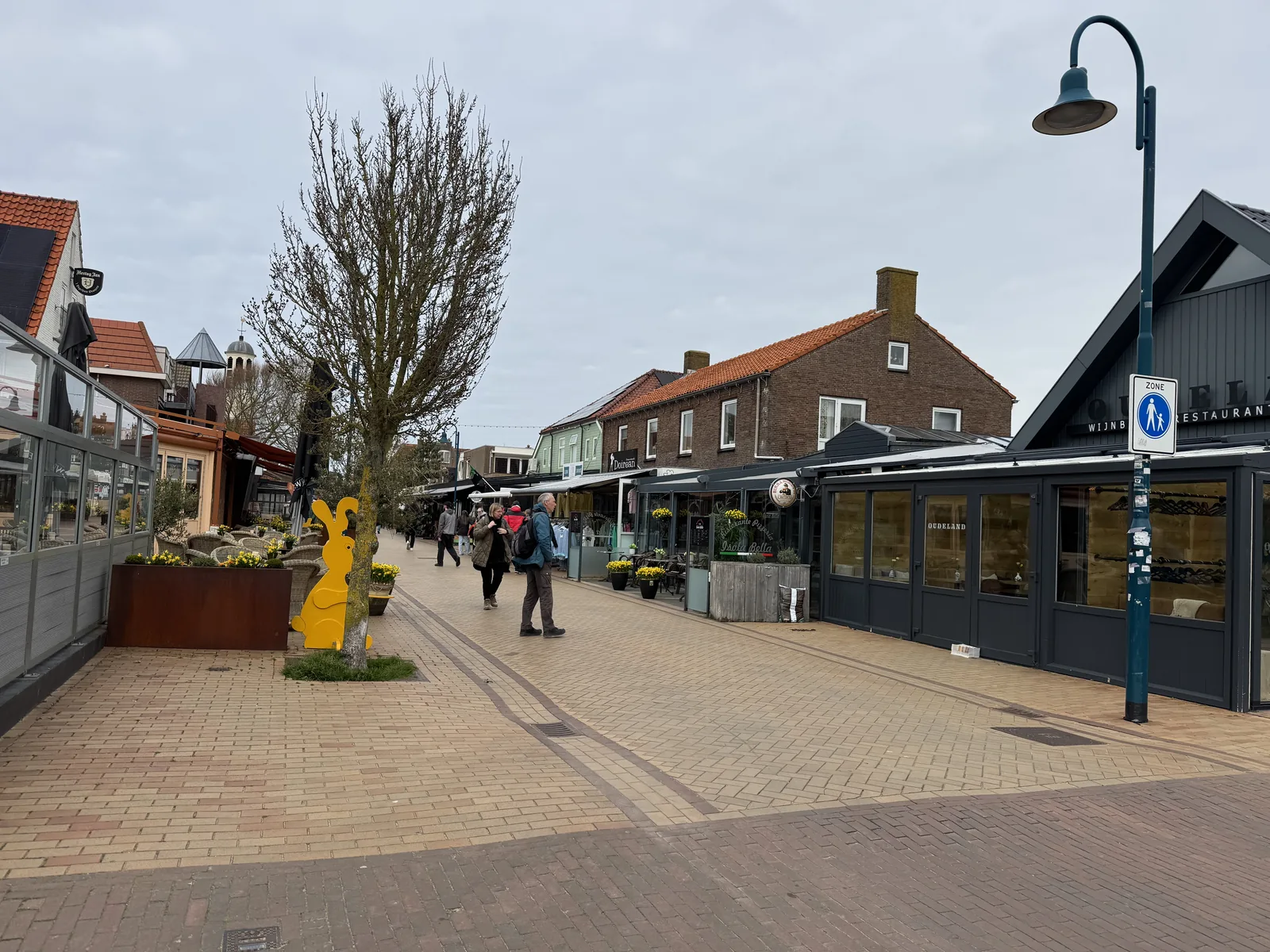 Einkaufs- und Restaurantstraße mit Backsteinhäusern und Laternen im Ort De Koog auf Texel, einzelne Passanten unterwegs