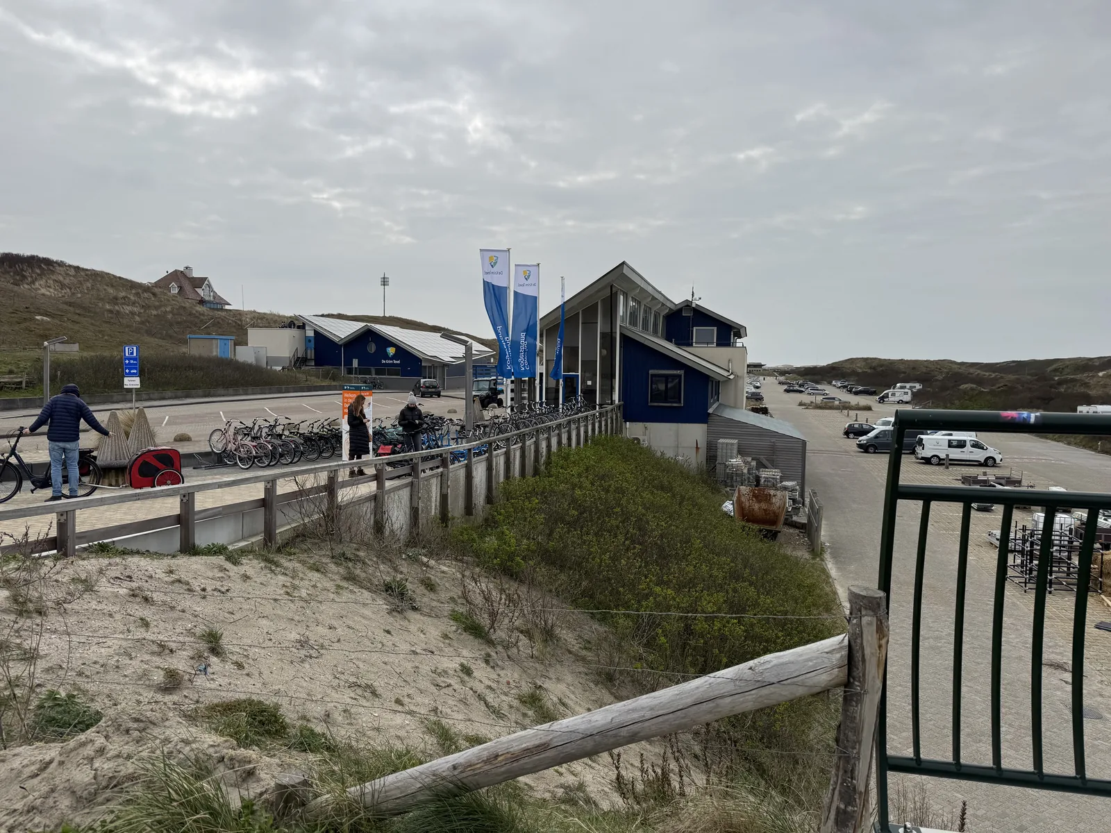 Blick über die Düne auf den Empfangsbereich von Camping Kogerstrand mit Fahrradständern, Fahnen und blauem Hauptgebäude