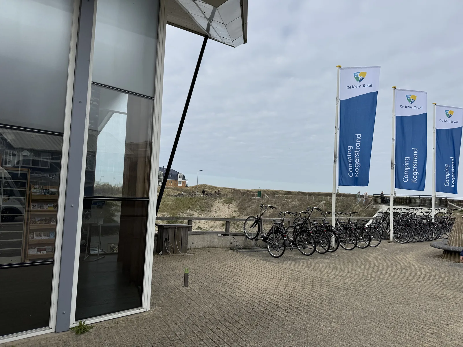 Gebäudeecke am Kogerstrand mit De-Krim-Flaggen für Ontvangst und Publiekstoiletten und langen Fahrradständern