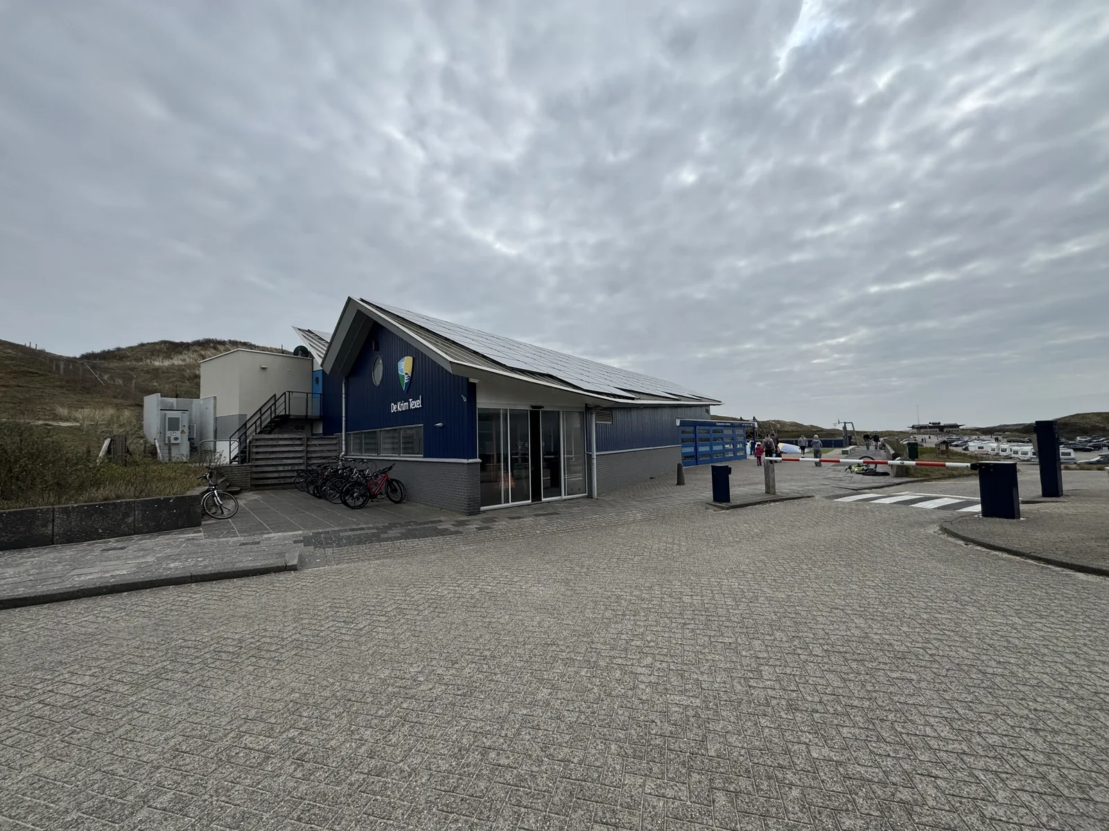 Rückwärtige Ansicht des Servicegebäudes von Camping Kogerstrand mit Zufahrt, Containern und angrenzender Düne