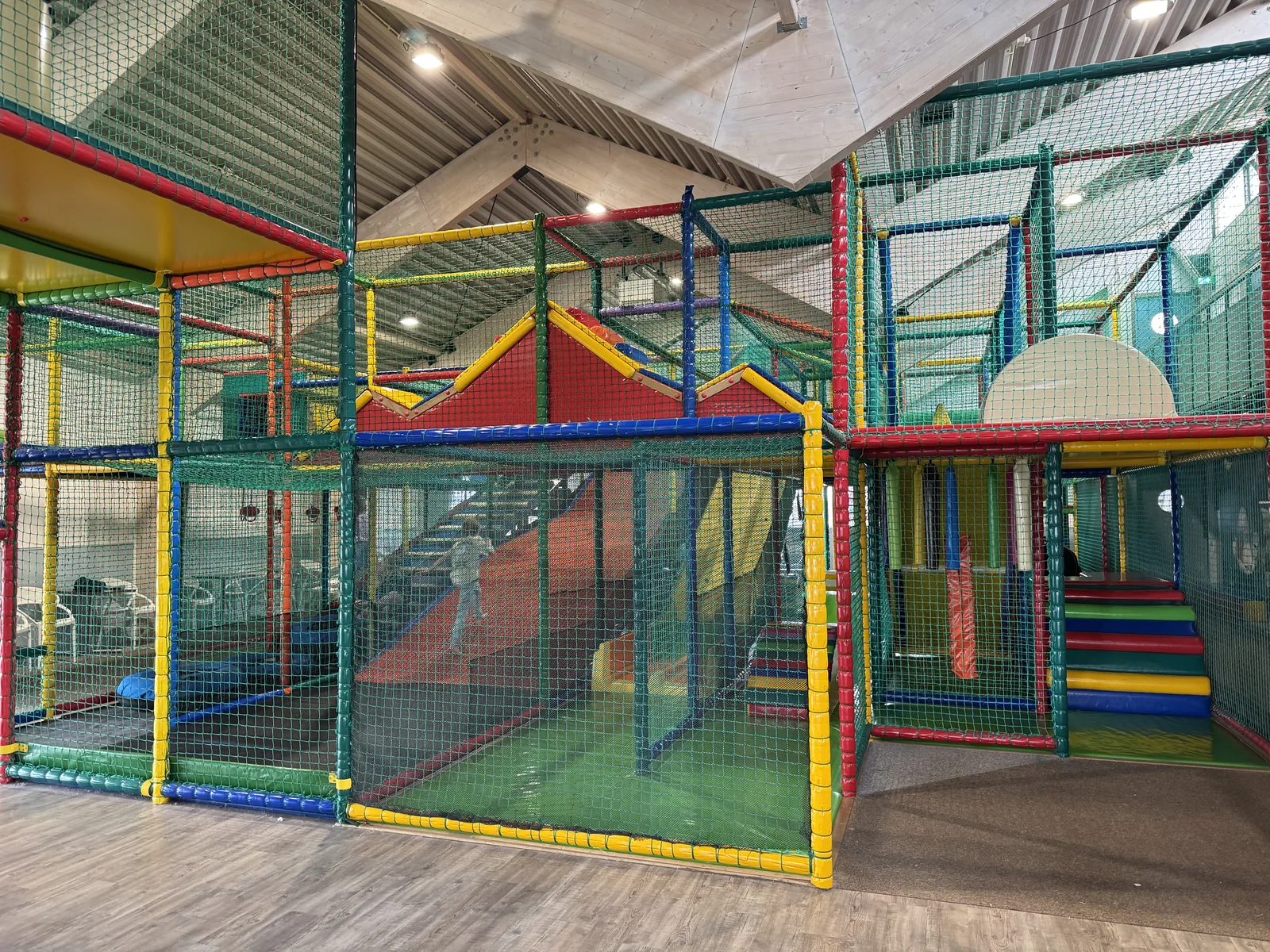 Mehrstöckiges Indoor-Spielgerüst in Grün, Gelb und Rot in der Halle von Camping Kogerstrand, davor freie Hallenfläche