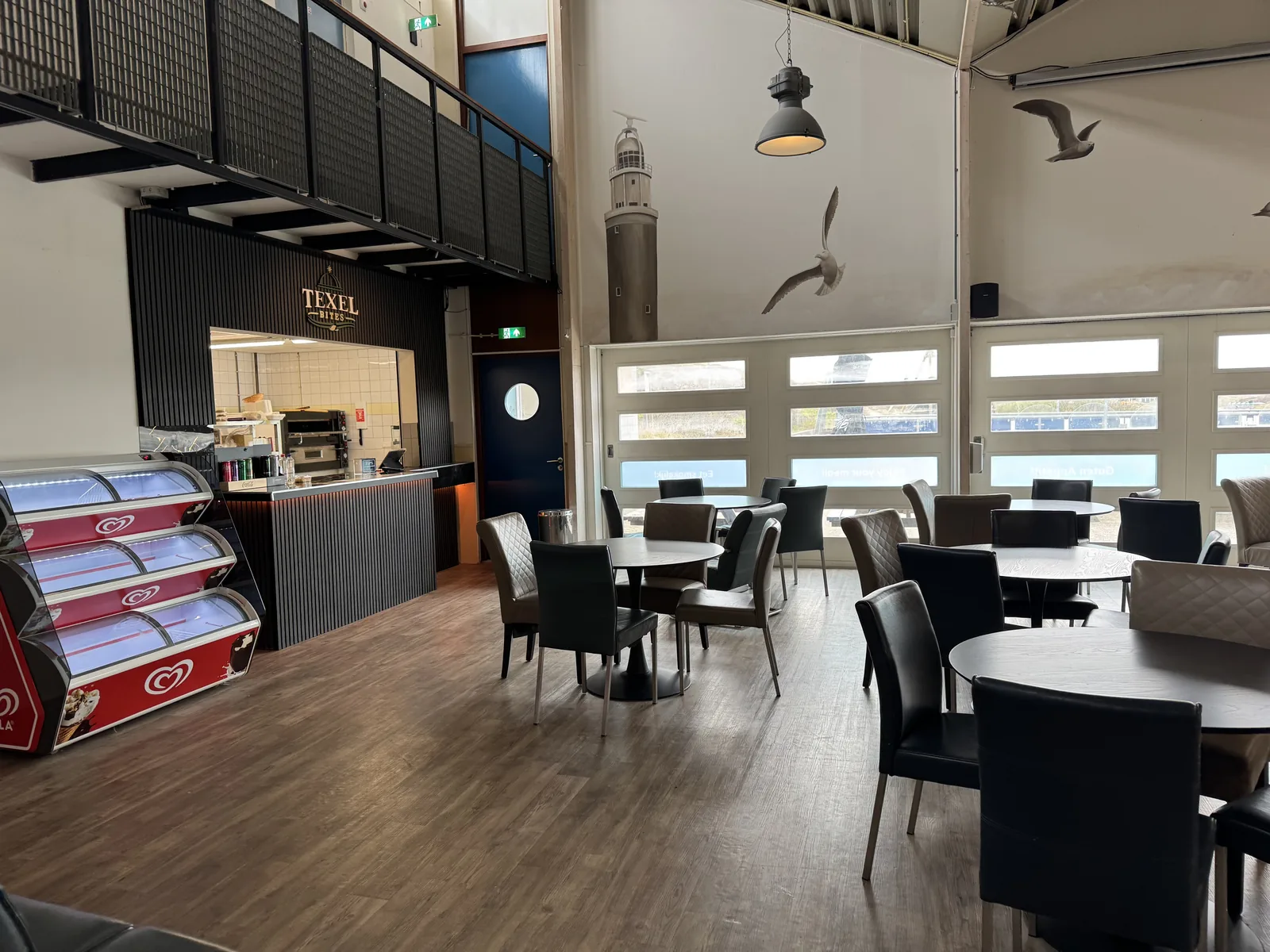 Restaurantbereich auf Camping Kogerstrand mit Theke, Eistruhen, Tischen und Stühlen unter hohem Dach mit Möwendeko