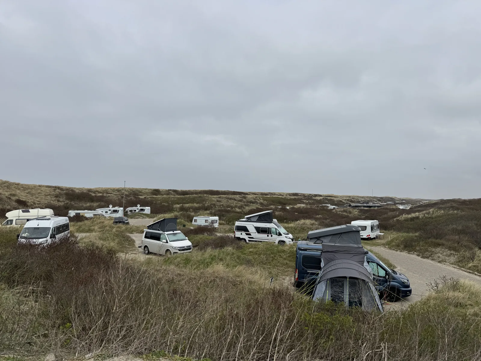 Stellplätze mit Wohnmobilen, Campingbussen und einem Vorzelt in einer Senke zwischen den Dünen auf Camping Kogerstrand
