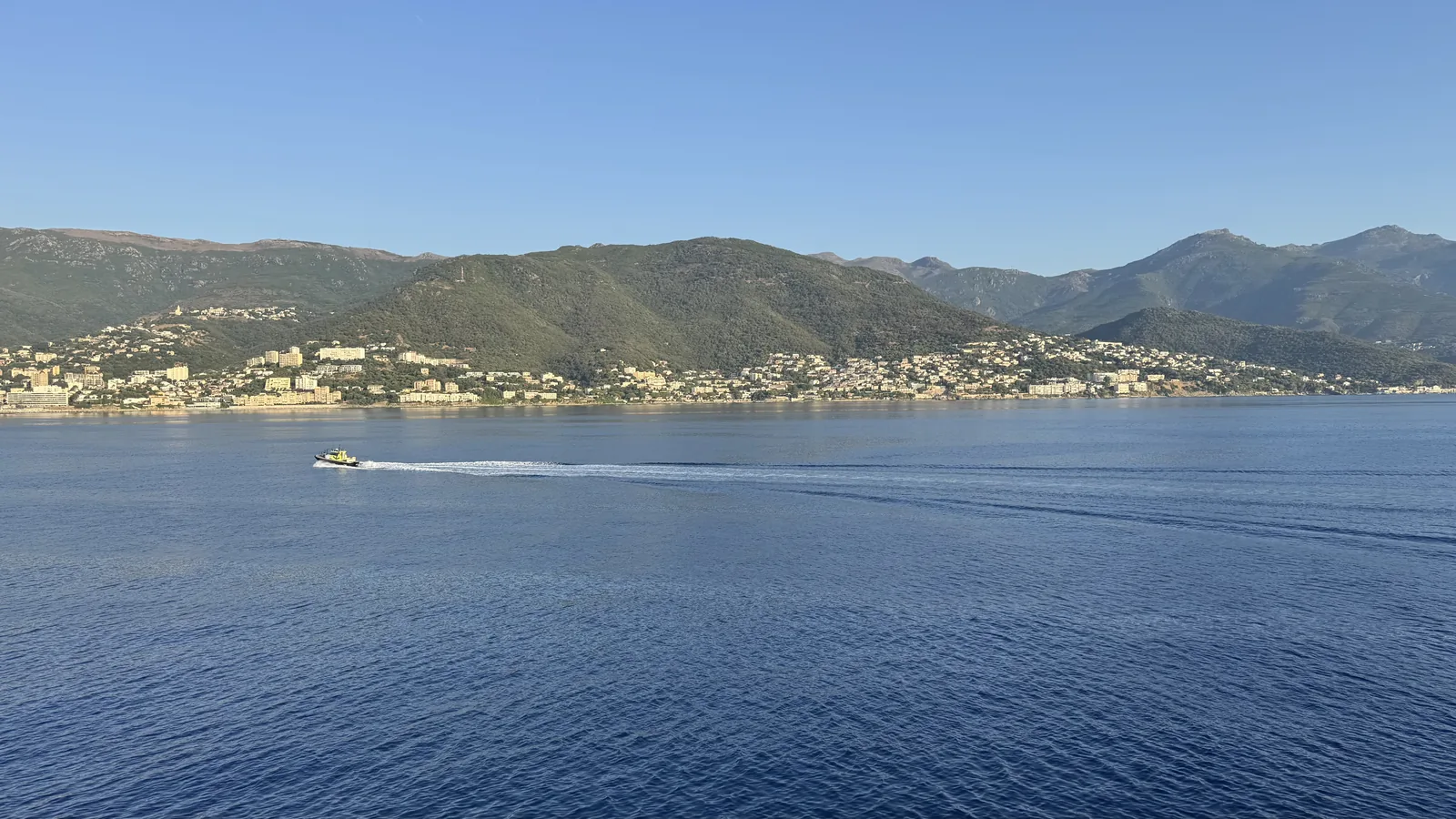 Blick von der Fähre über das ruhige Meer auf die grüne Küste Korsikas bei der Ankunft