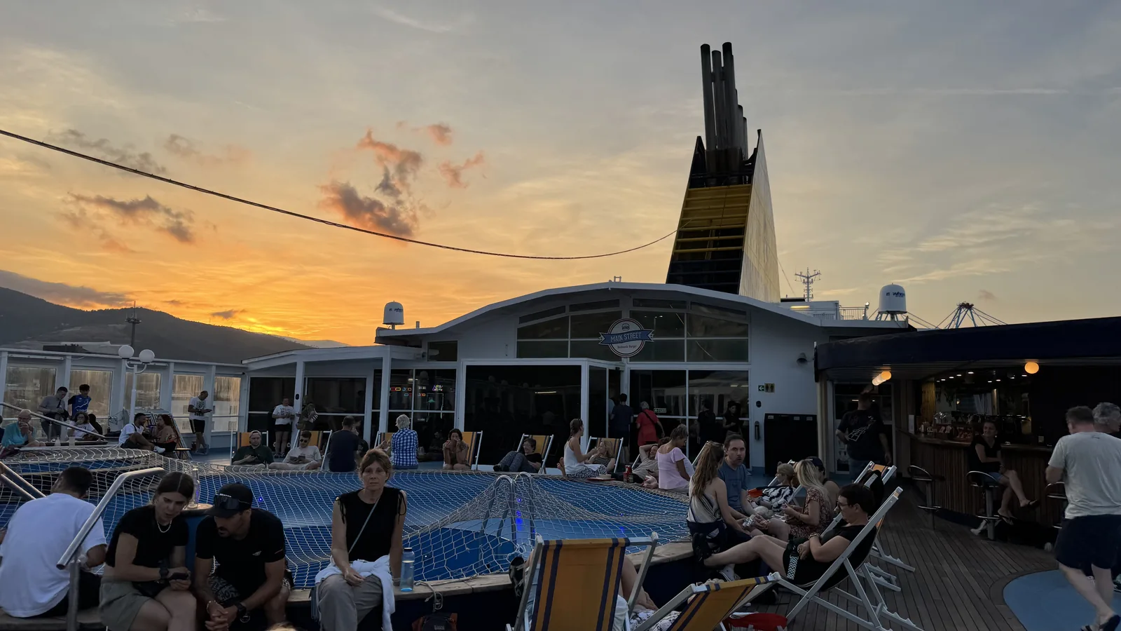 Menschen auf dem Sonnendeck der Fähre im Abendlicht, im Hintergrund die Schornsteine