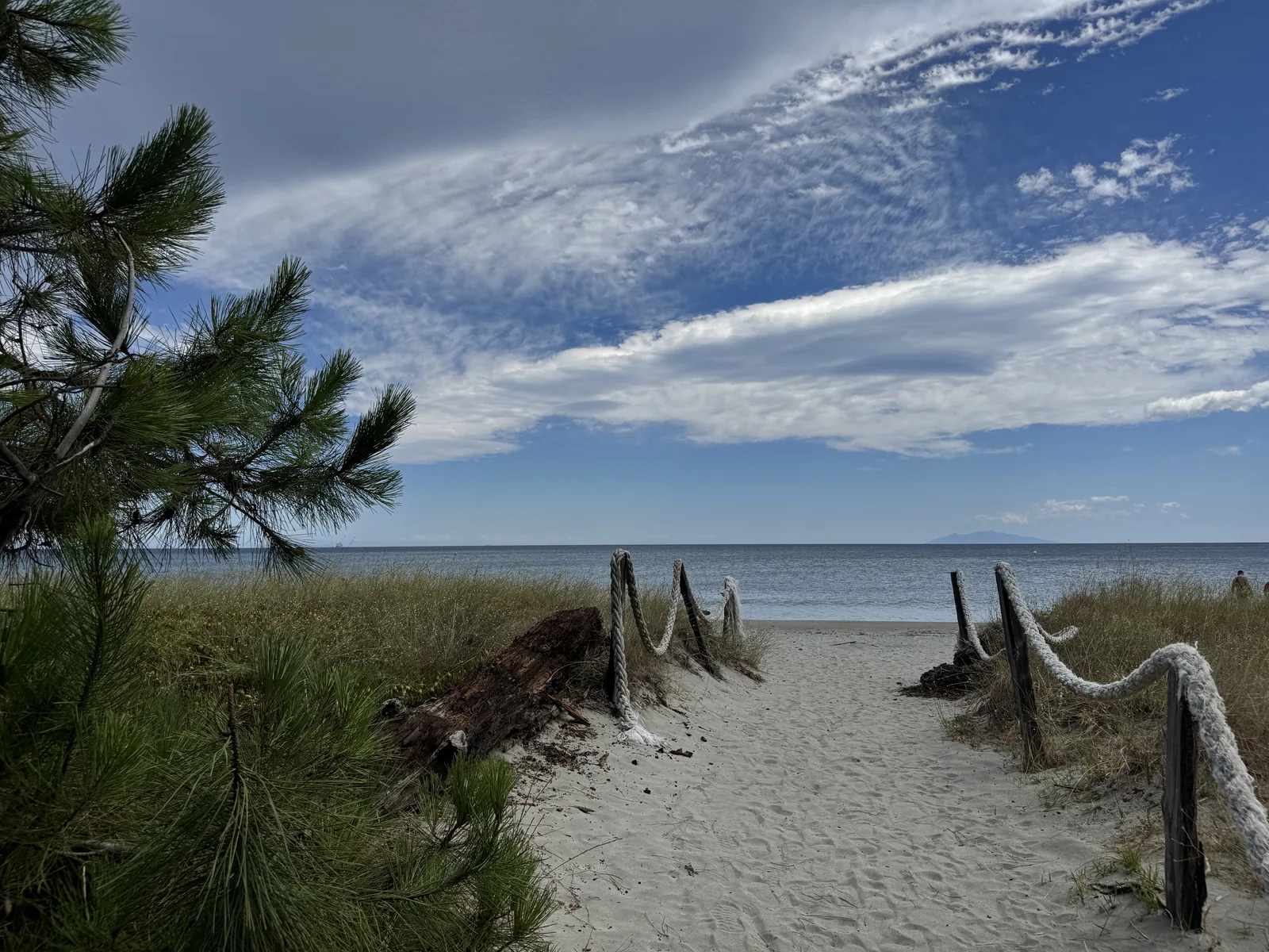 Sandiger Weg zwischen Dünengräsern zum flachen, ruhigen Meer am Camping San Damiano auf Korsika
