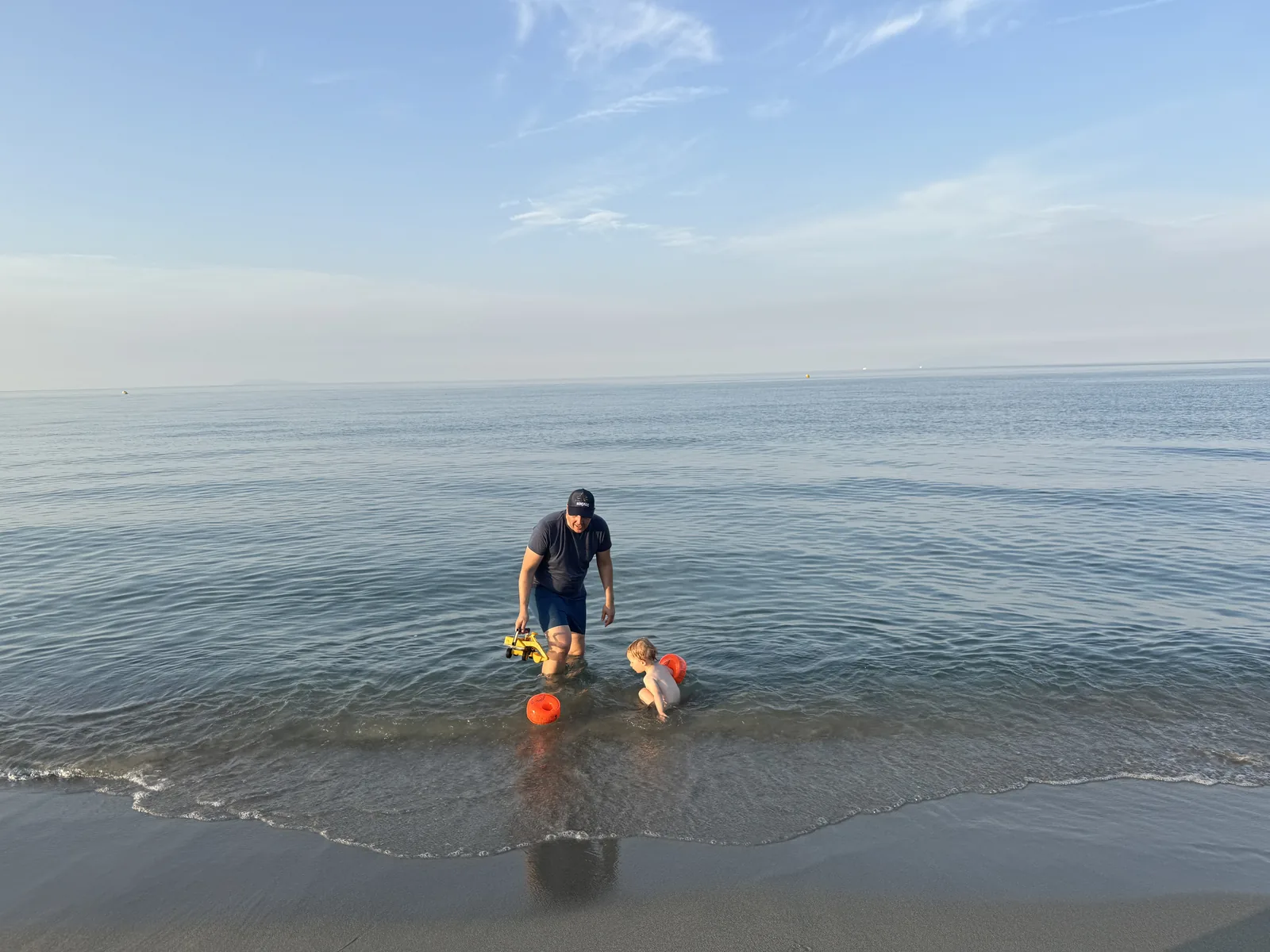 Patrick und der Kleine spielen im knöcheltiefen, ruhigen Wasser am flachen Sandstrand von San Damiano