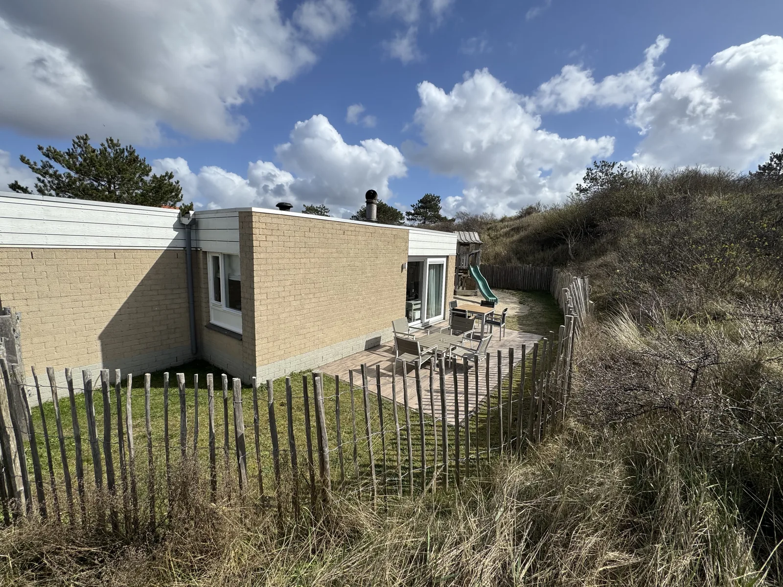 Helle Ferienhauszeile der Beach Chillas im Center Parcs Park Zandvoort hinter einem Holzzaun, dahinter Dünen