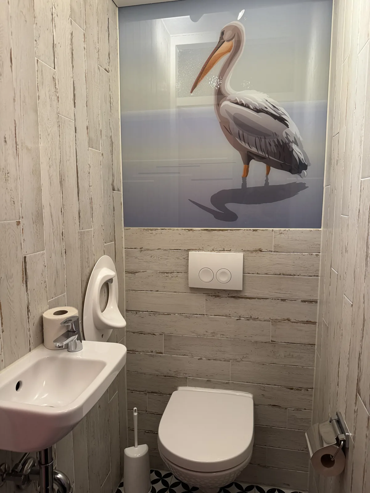 Gäste-WC der Beach Chilla mit Handwaschbecken und gerahmtem Pelikan-Bild an der Holzwand