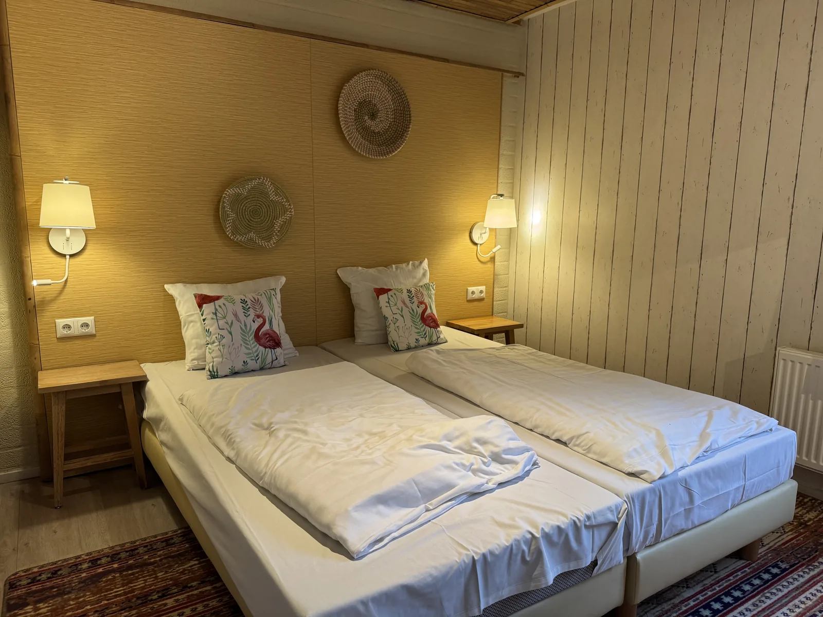 Schlafzimmer der Beach Chilla mit großem Bett, Wandleuchten und heller Holzverkleidung im Abendlicht