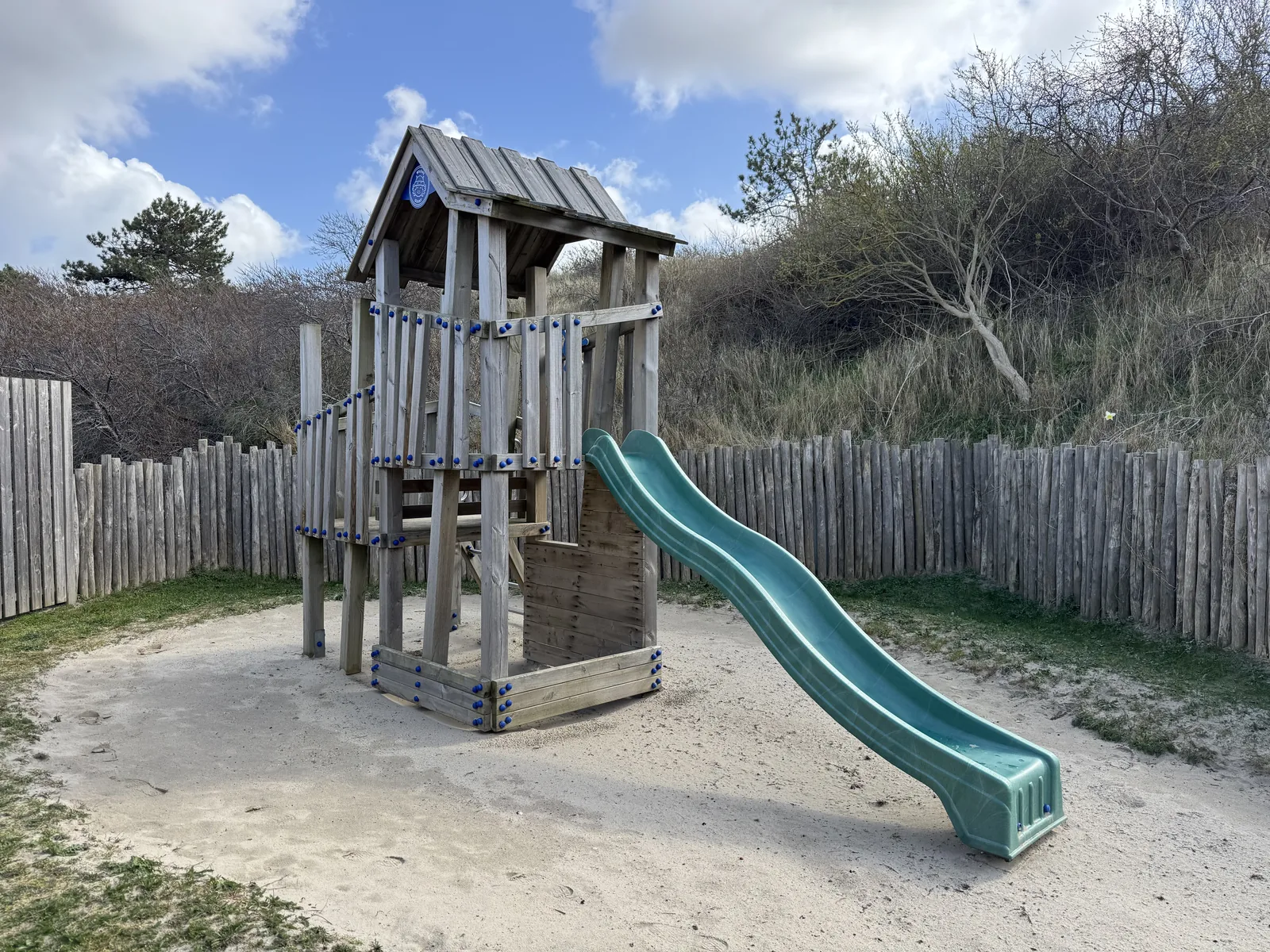Spielturm mit türkiser Rutsche vor Dünengras unter blauem Himmel im Center Parcs Park Zandvoort