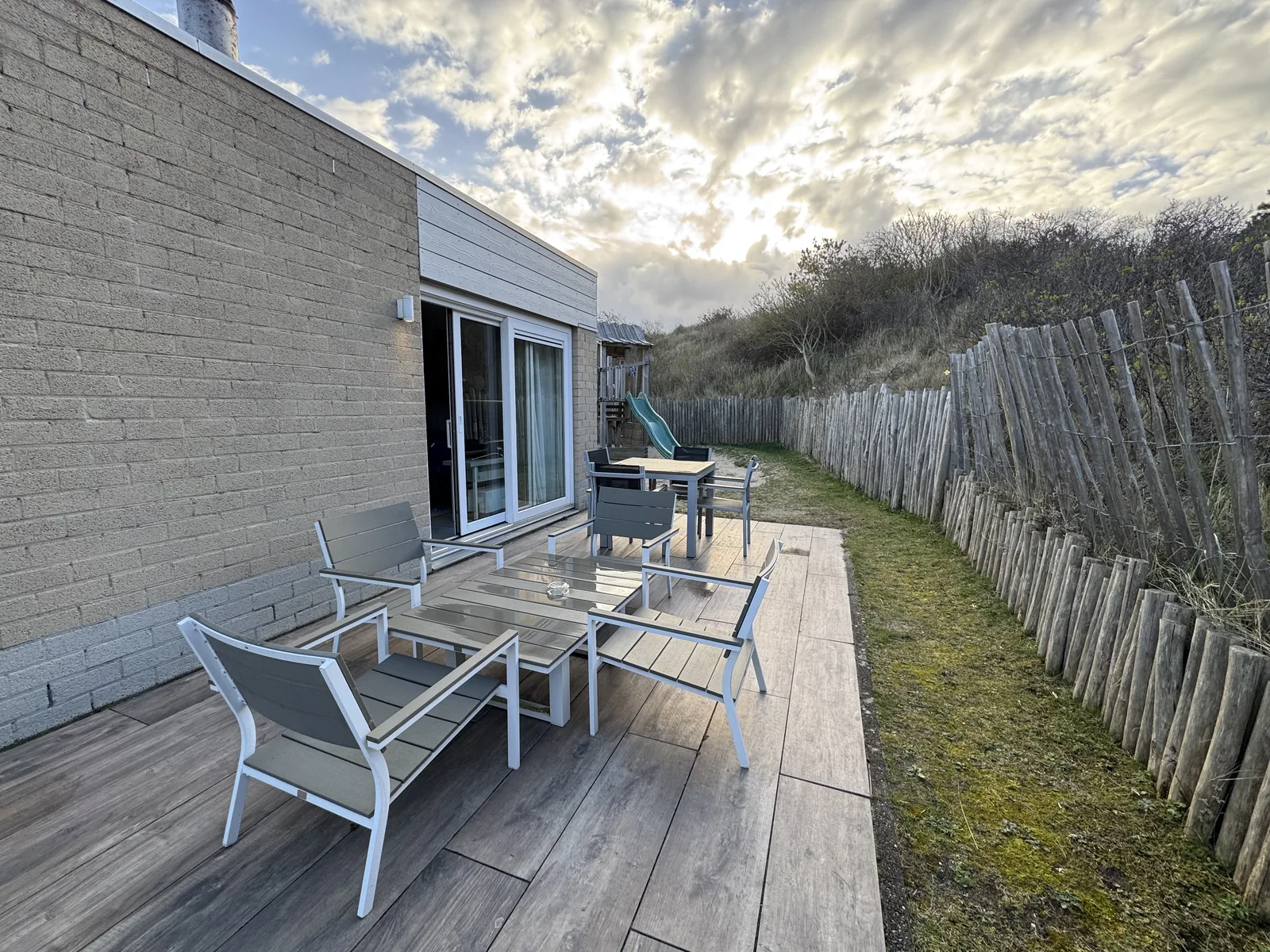 Holzterrasse am Beach-Chilla-Ferienhaus mit Tisch und Gartenstühlen im Morgenlicht