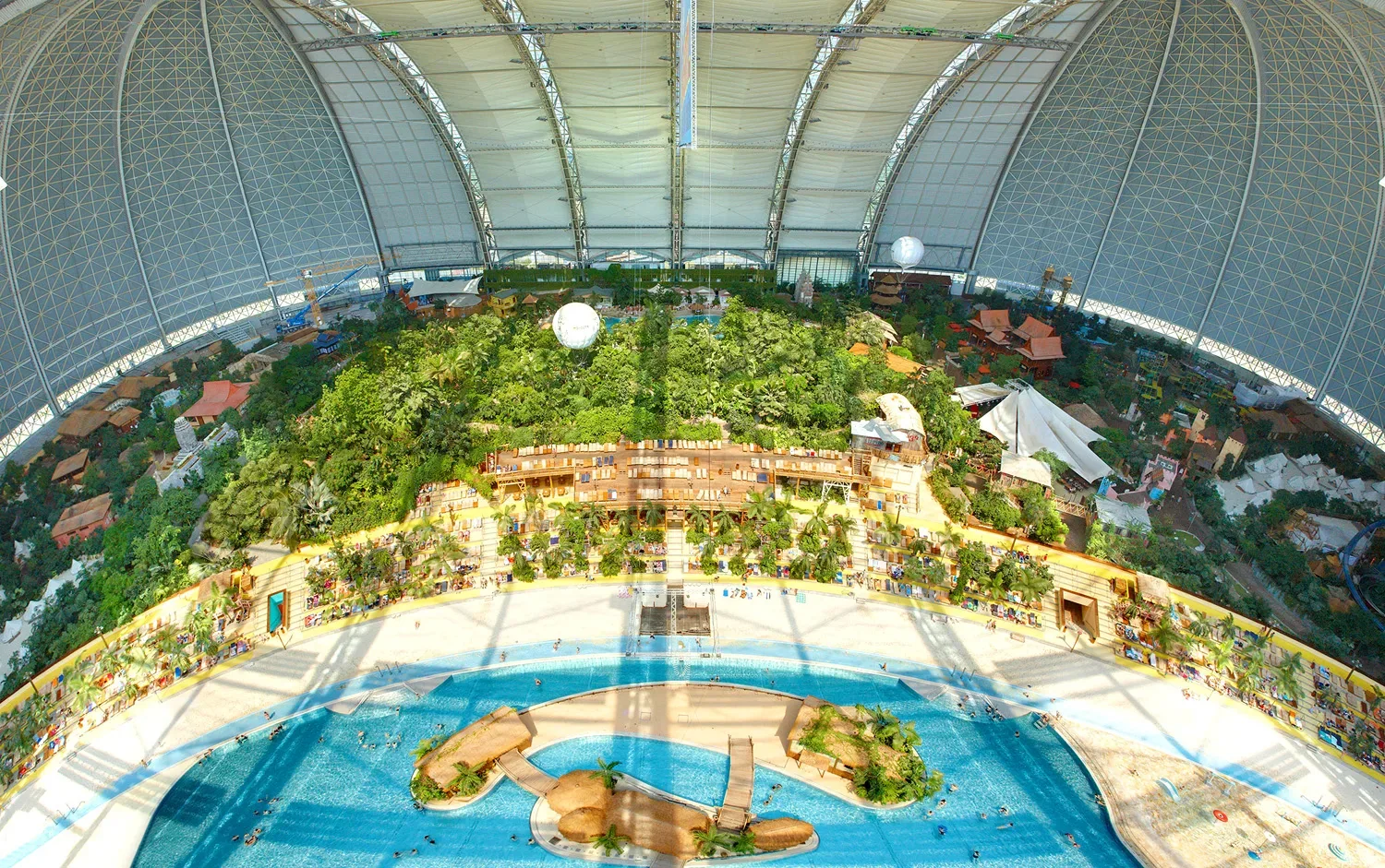 Blick von oben in die Halle des Tropical Islands: Kuppeldach, Sandstrand, Lagune und dichtes Grün