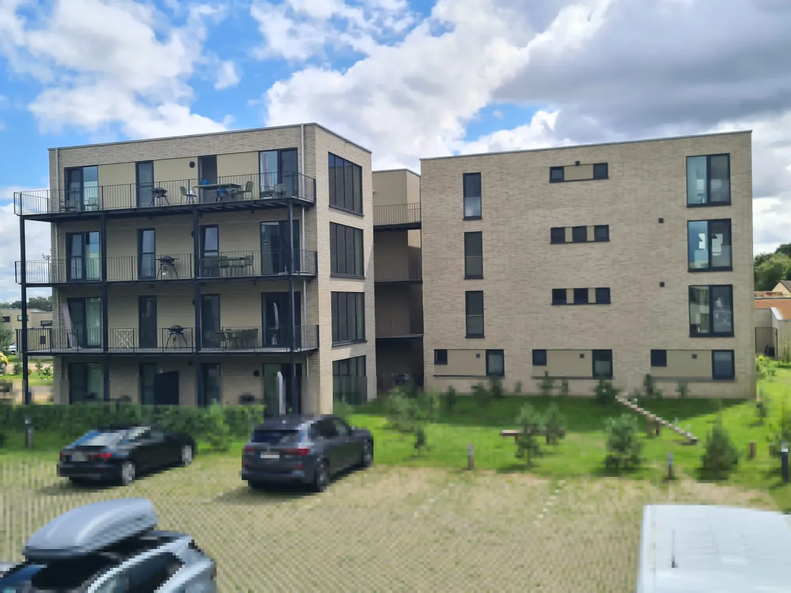 Zwei vierstöckige Apartmenthäuser im Marissa Ferienpark mit Balkonen, davor Parkplätze und junge Bepflanzung