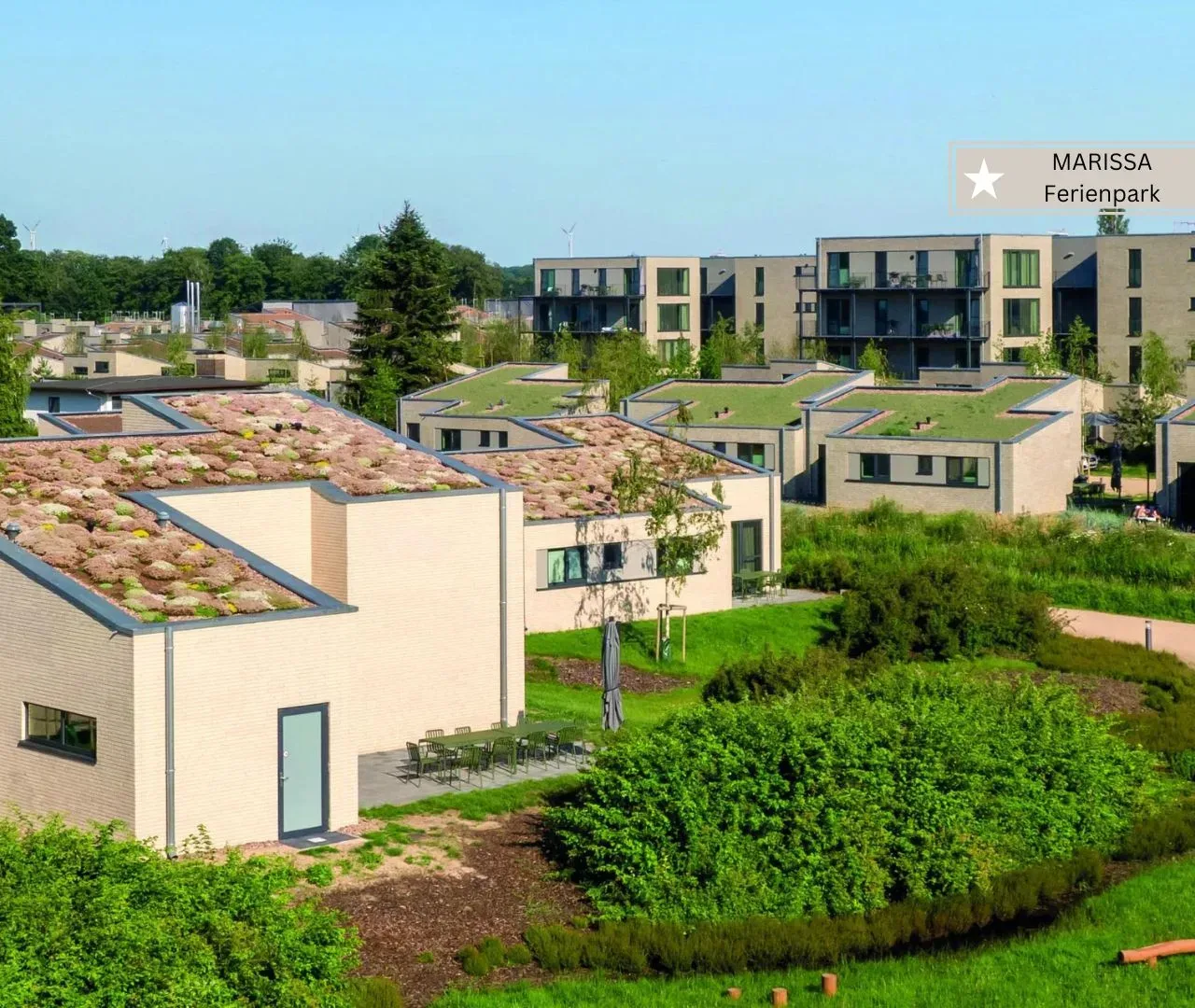 Ferienhäuser mit begrünten Dächern, dahinter die vierstöckigen Apartmenthäuser des Marissa Ferienparks