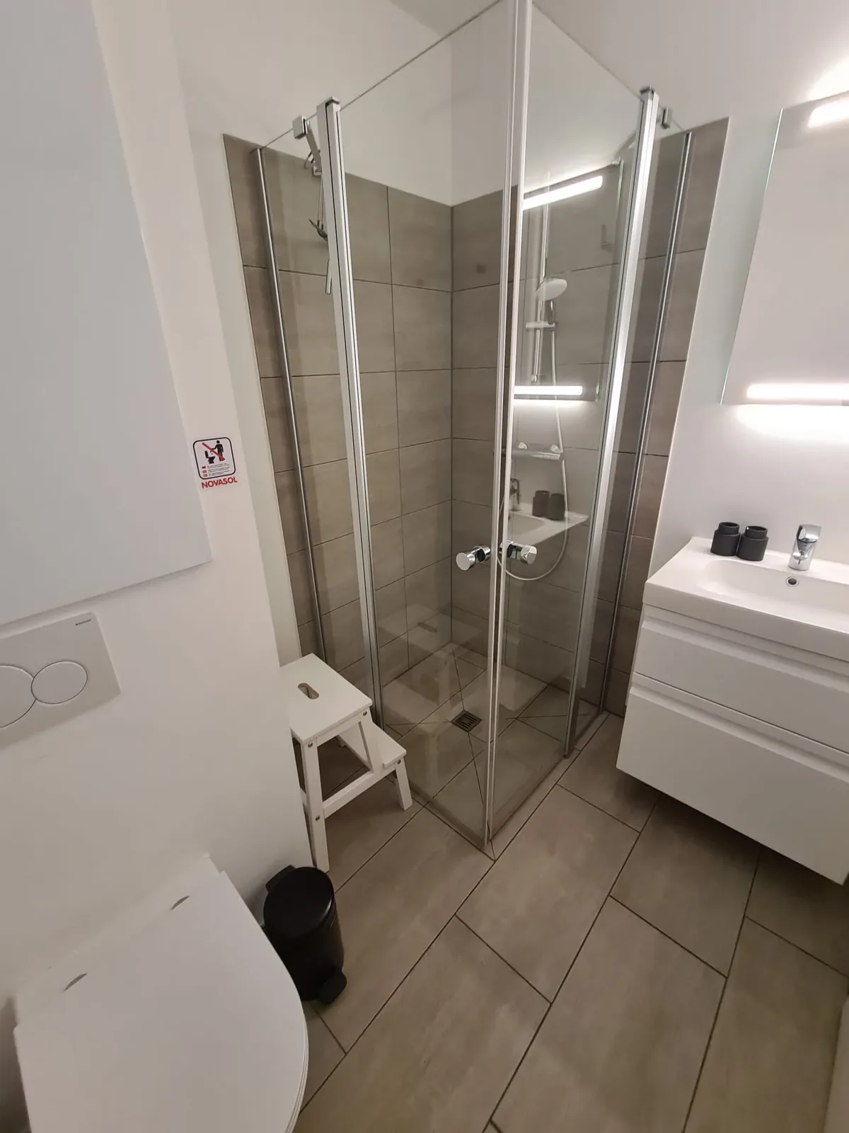 Badezimmer mit Eckduschkabine, Waschtisch und einem kleinen Trittschemel vor der Dusche
