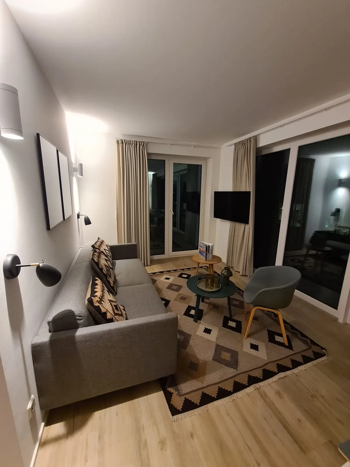 Wohnzimmer einer Ferienwohnung im Marissa Ferienpark mit Sofa, Sessel, Teppich und Fernseher an der Wand