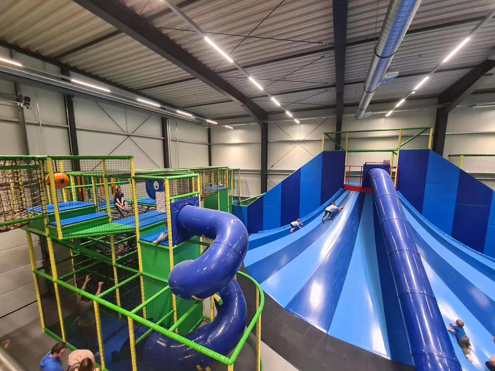Breite blaue Wellenrutsche und Klettergerüst mit Trampolinen in der Halle von Lykkeland am Marissa Ferienpark