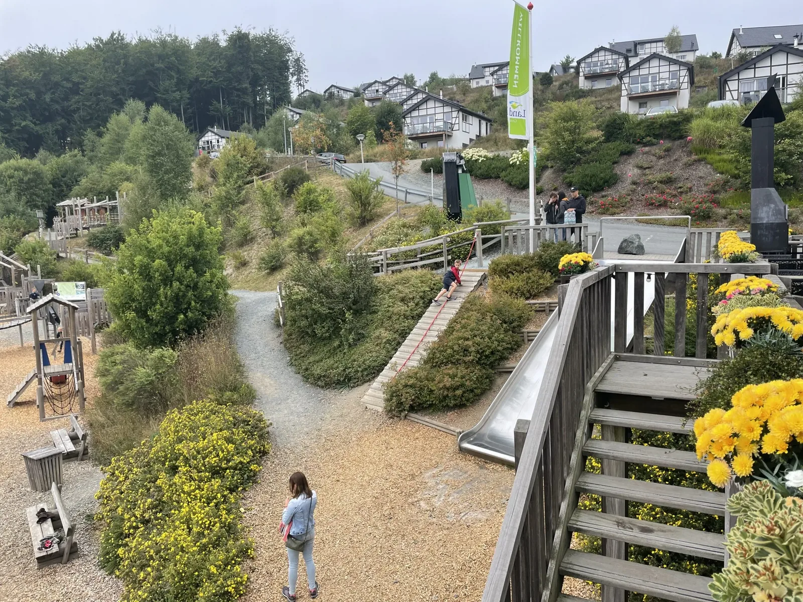 Spielplatz im Landal Winterberg mit Rutsche und Kletteranlage, dahinter Ferienhäuser am Hang