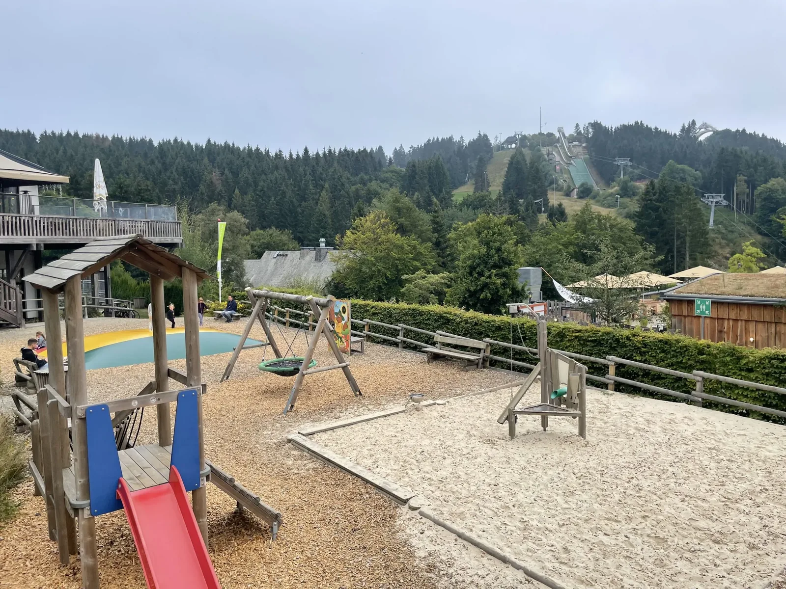 Blick vom Spielplatz des Landal Winterberg auf Nestschaukel, Hüpfkissen und die Skischanzen