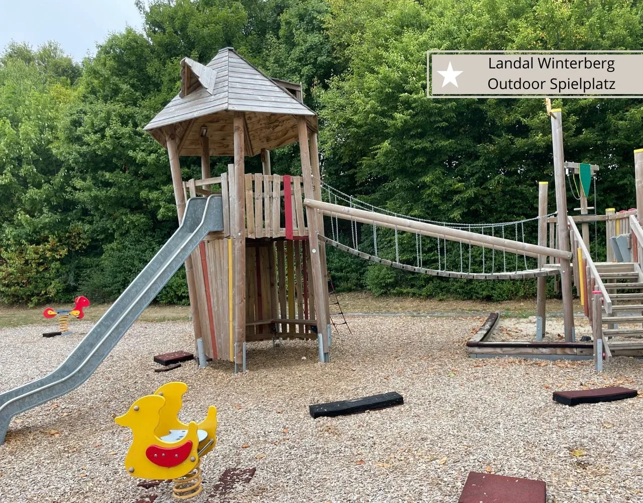 Spielturm mit Rutsche, Hängebrücke und Wippfiguren auf dem Spielplatz für kleine Kinder