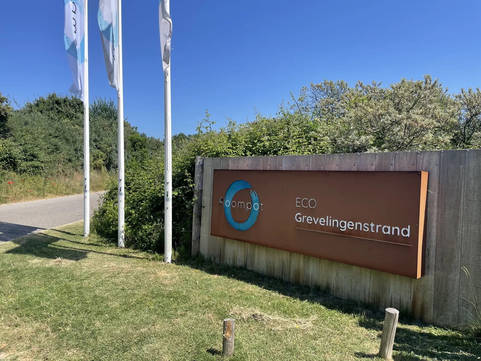 Cortenstahl-Schild an der Zufahrt mit dem Schriftzug ECO Grevelingenstrand und drei Fahnenmasten