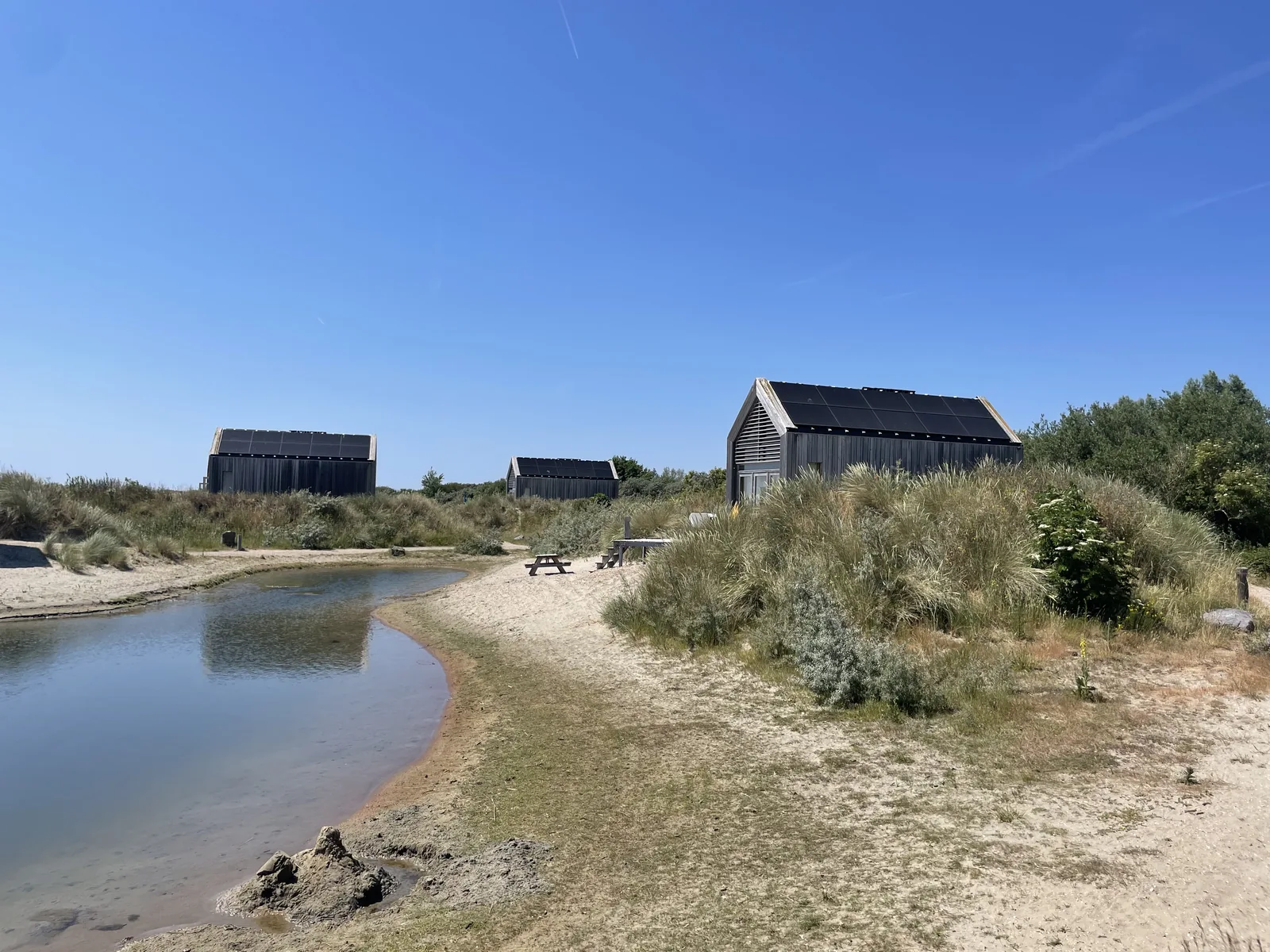 Flache Bucht am Grevelingenmeer, dahinter auf der Düne drei dunkle Holz-Ferienhäuser des Landal ECO Grevelingenstrand