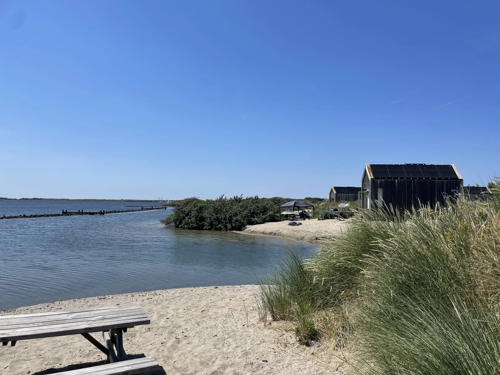 Sandbank mit Strandhafer, auf der gegenüberliegenden Landzunge ein großes dunkles Ferienhaus im Scheunenstil