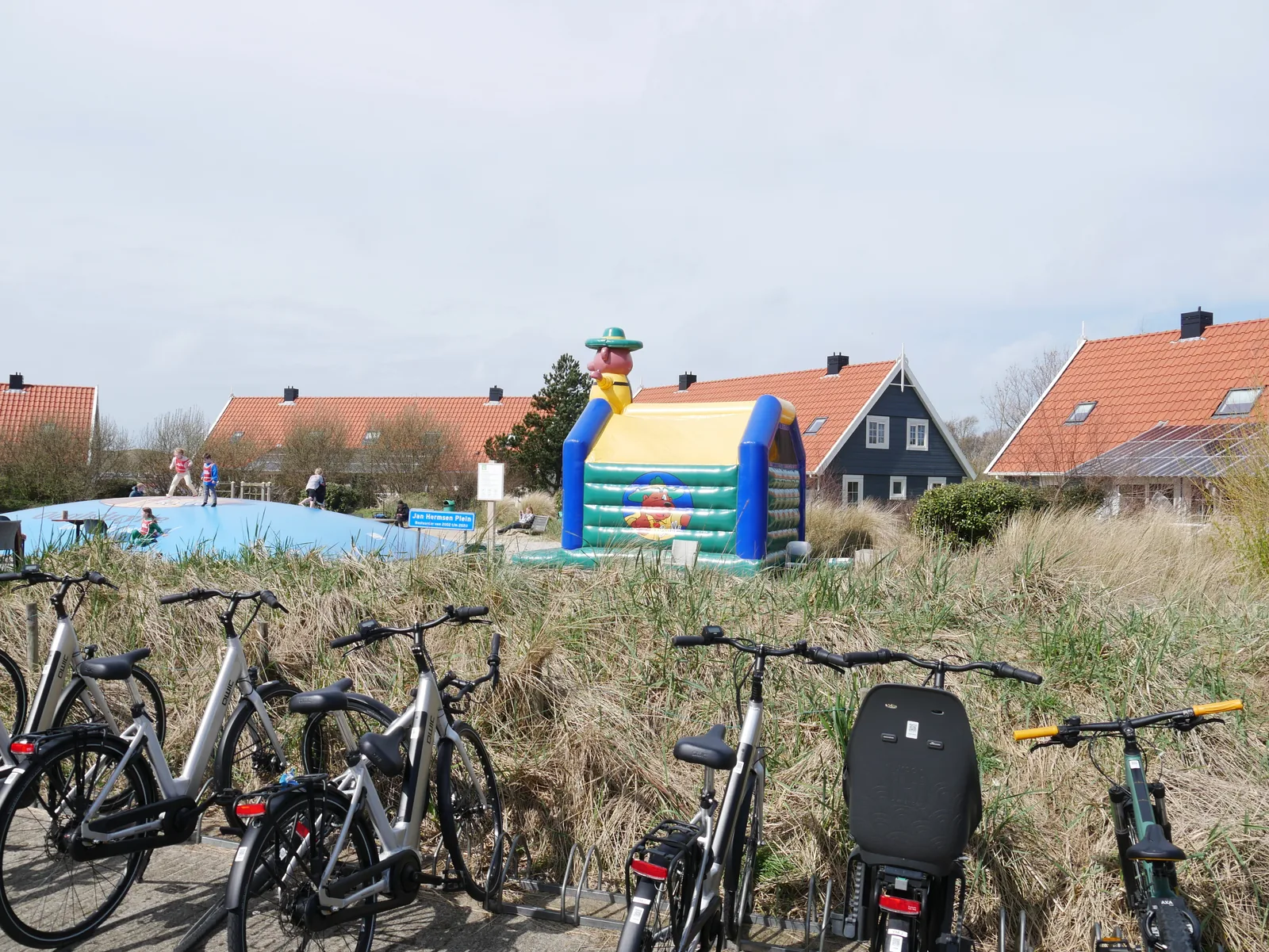 Aufblasbare Hüpfburg auf einem Sandspielplatz zwischen Dünengras, dahinter Ferienhäuser mit roten Dächern