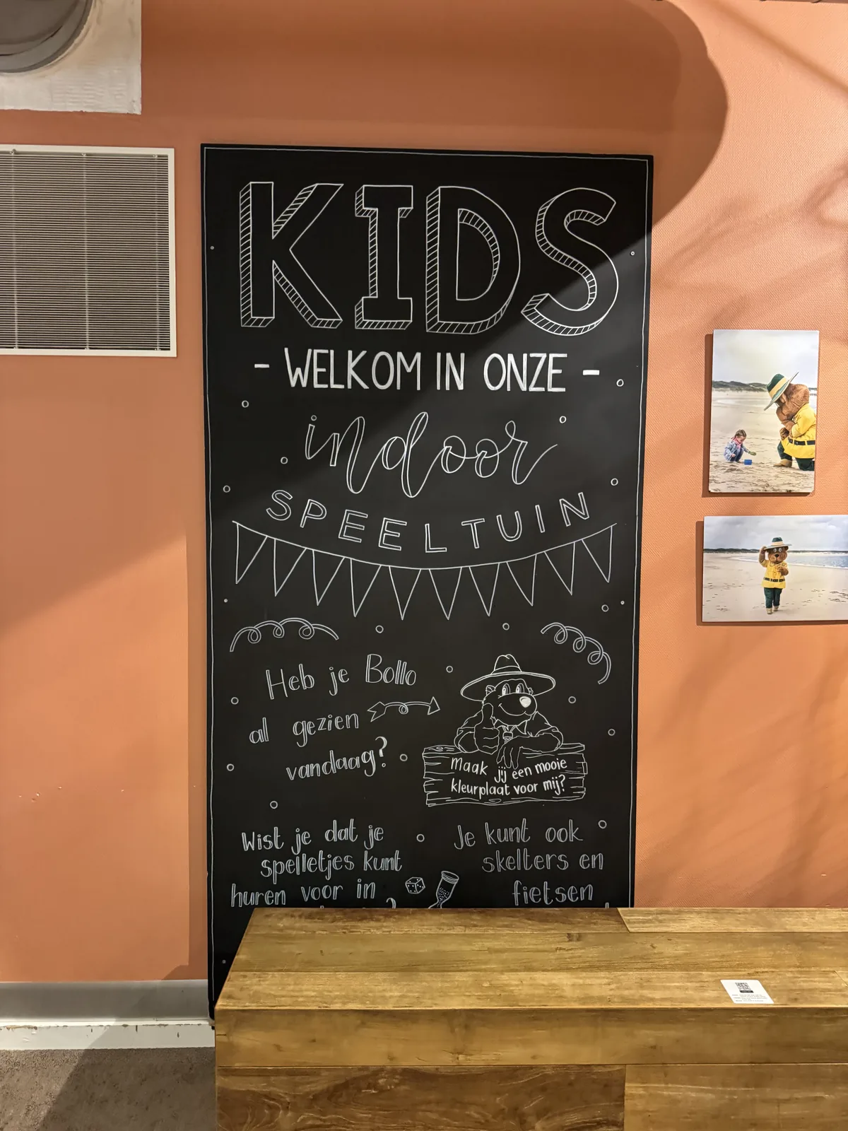 Große Kreidetafel an oranger Wand mit der Aufschrift „KIDS – welkom in onze indoor speeltuin“